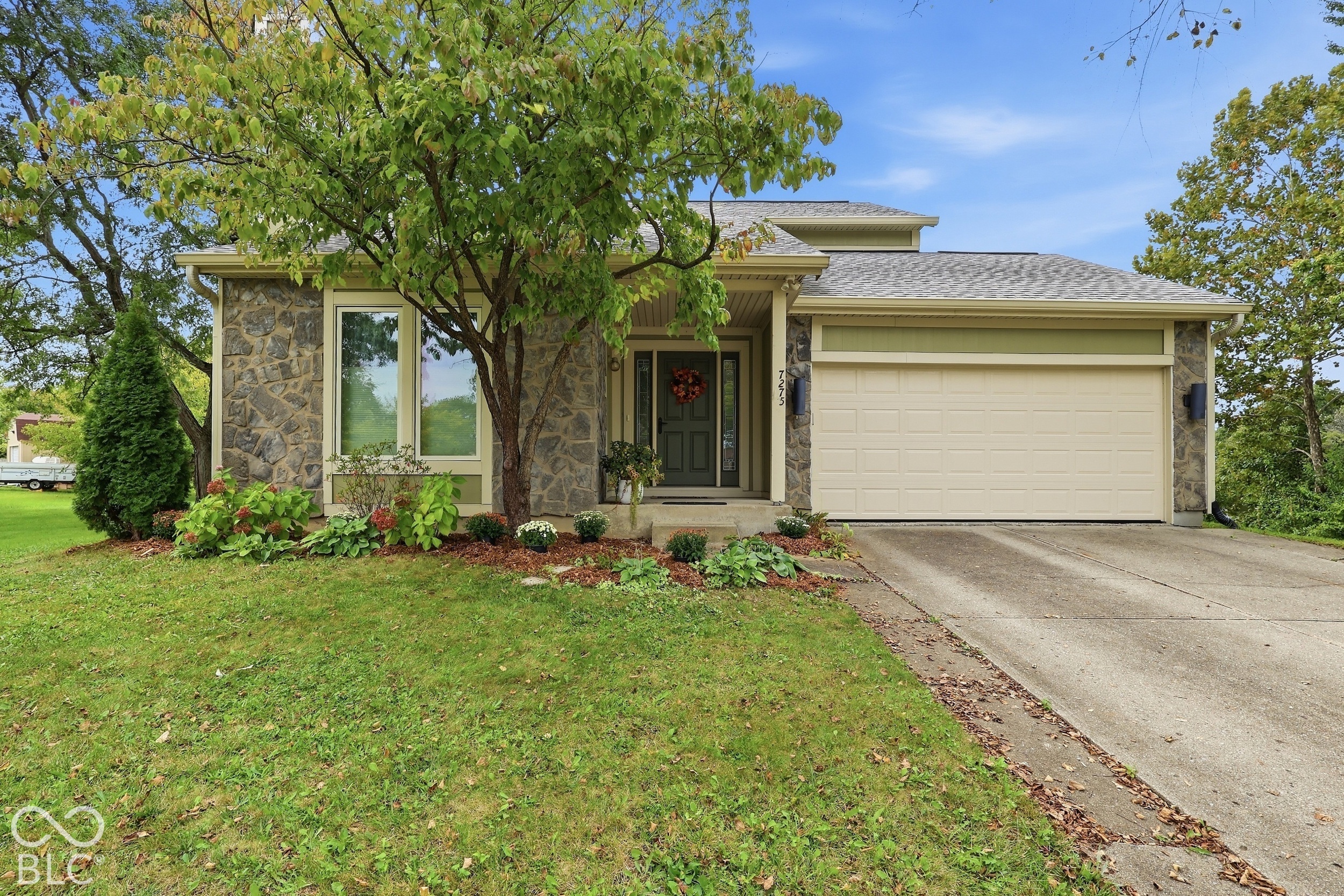 Exterior featuring a split-level facade with stone veneer, horizontal siding, a concrete driveway, an attached garage, and landscaped garden beds