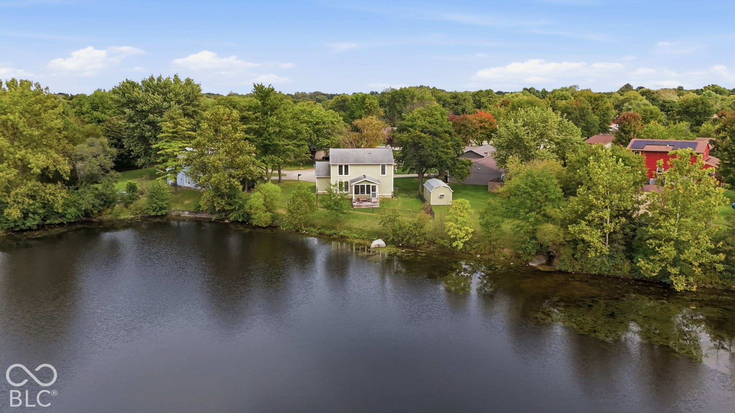Waterfront property featuring a two-story residence, expansive lawn, mature trees, and a detached outbuilding