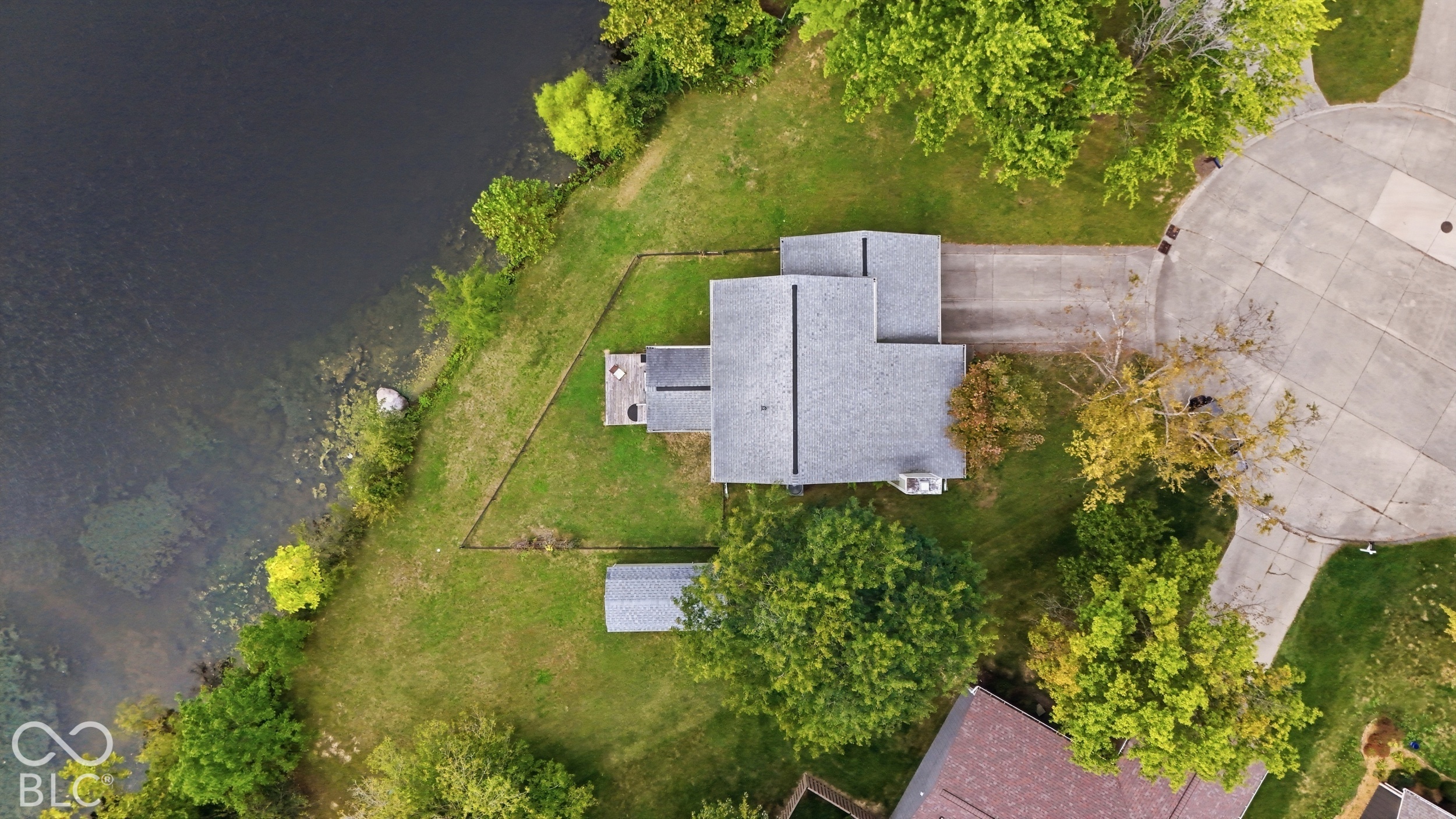 Waterfront lot featuring a multi-level deck, detached storage structure, concrete driveway, and mature landscaping