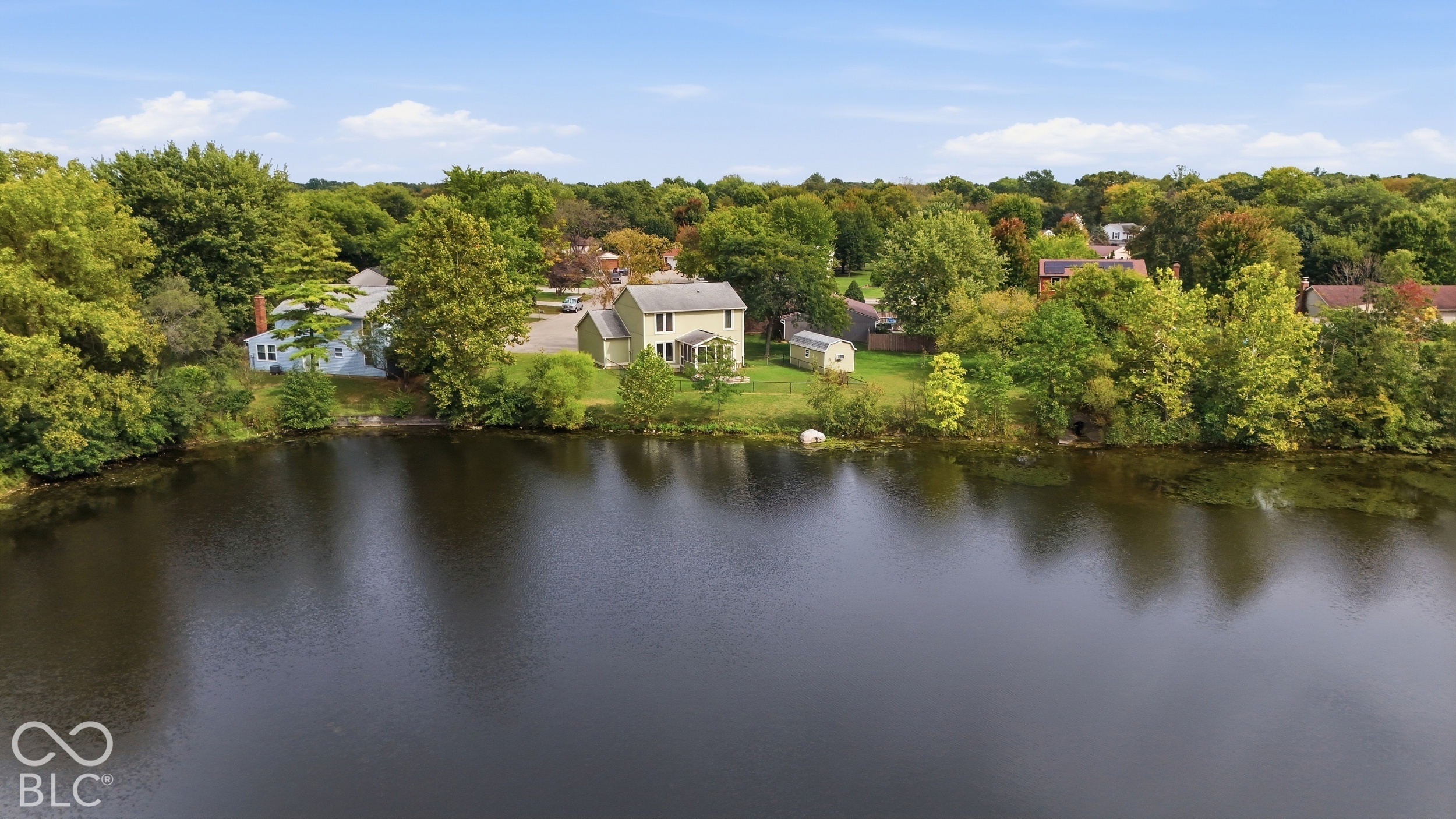 Waterfront property featuring a two-story residence, expansive rear lawn, and mature trees