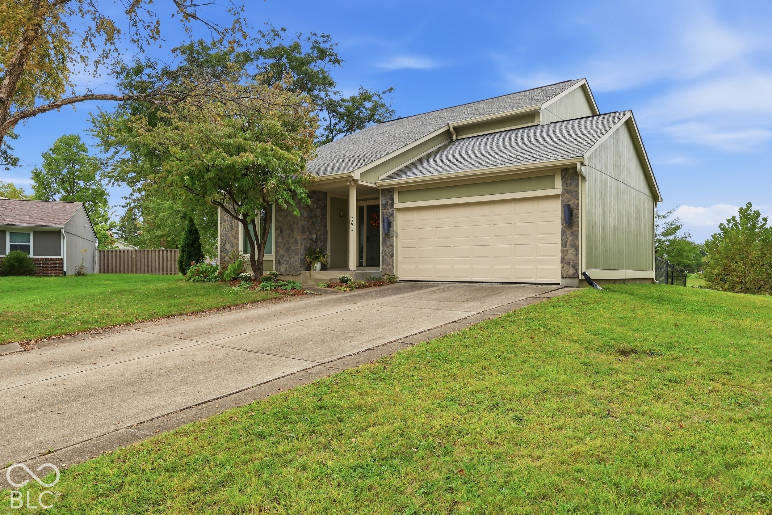 Multi-level exterior featuring vertical siding, stone masonry accents, a paved concrete driveway, and an attached two-car garage