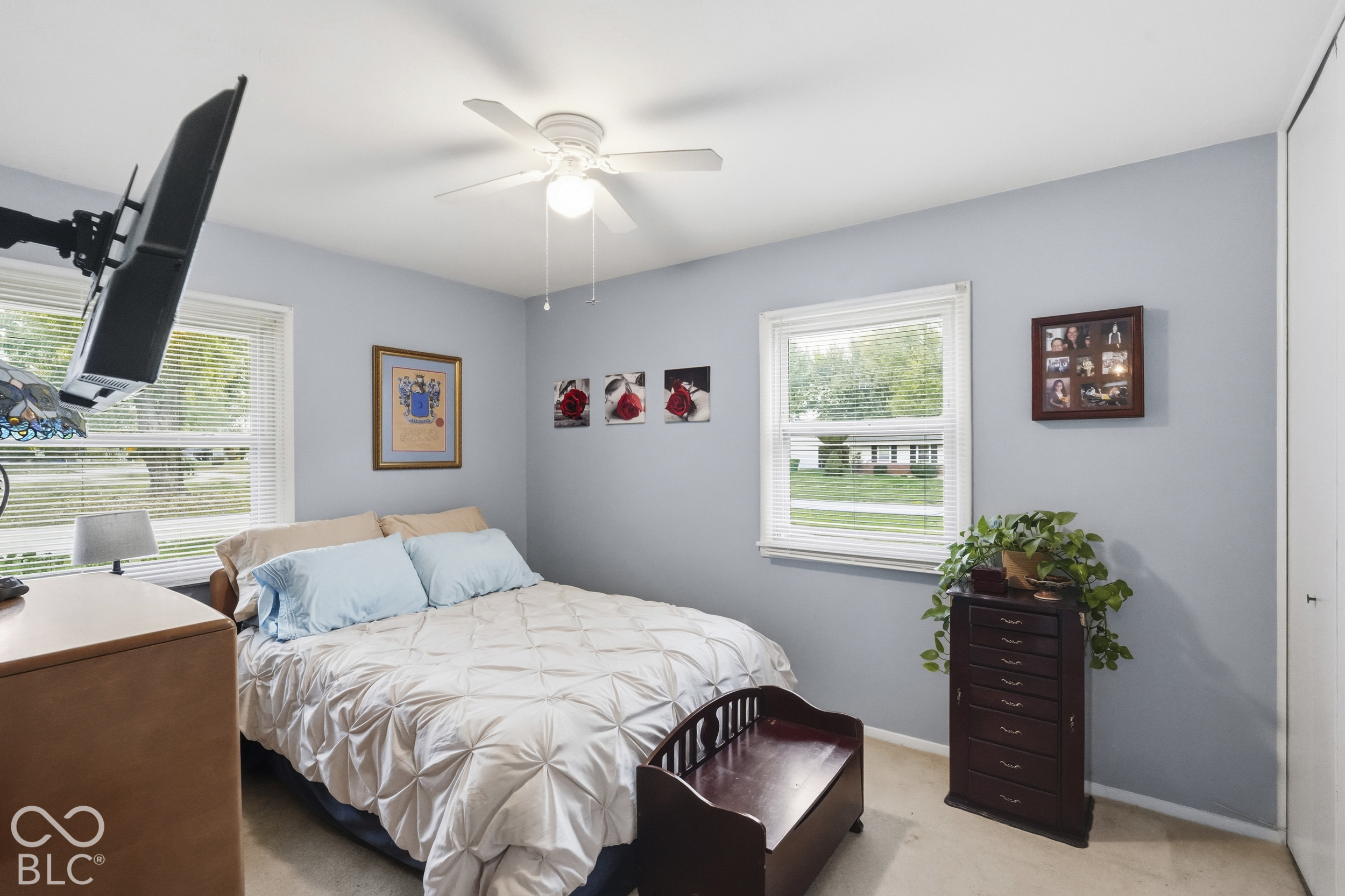 This corner bedroom has a ceiling fan with light fixture, dual windows, and closet with sliding doors. The floor is carpeted.