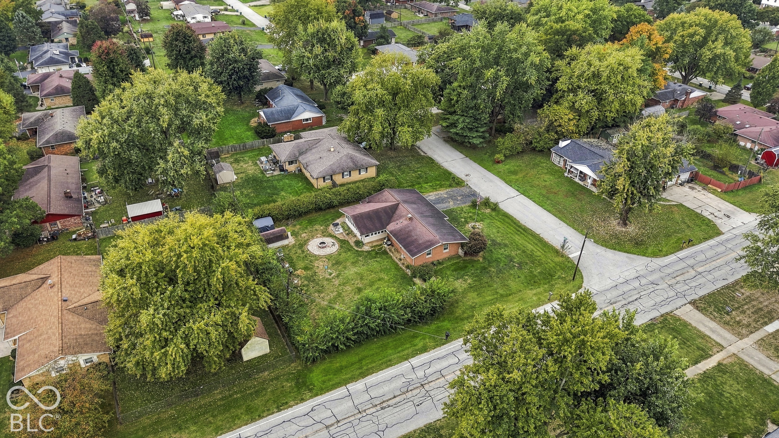 Aerial perspective featuring a brick exterior residence, a circular stone fire pit, mature trees, and an expansive lawn