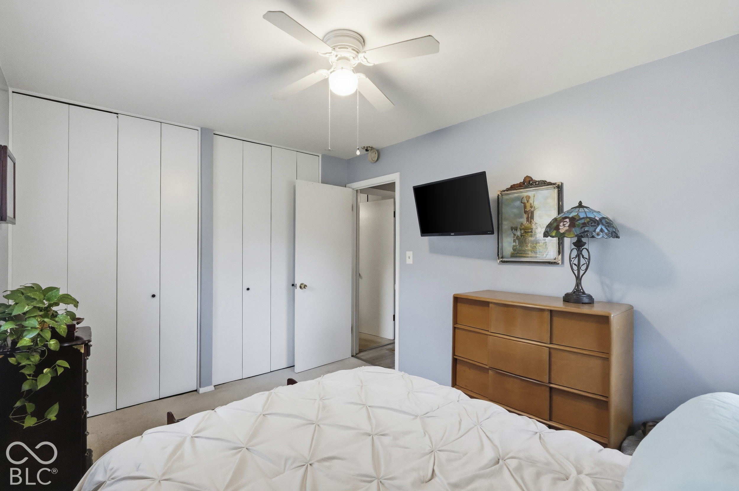 Another view of the bedroom featuring white bi-fold closet doors and a ceiling fan with integrated light fixture. The floor is carpeted.