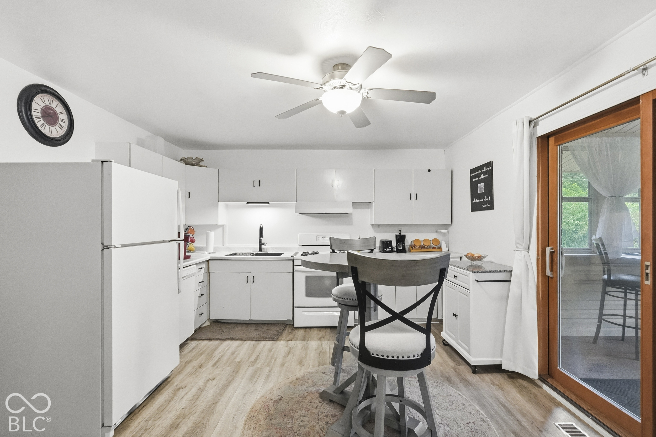 Kitchen featuring white cabinetry, vinyl plank flooring, the range, the top-freezer refrigerator, and a sliding glass door that leads to the spacious sun room.