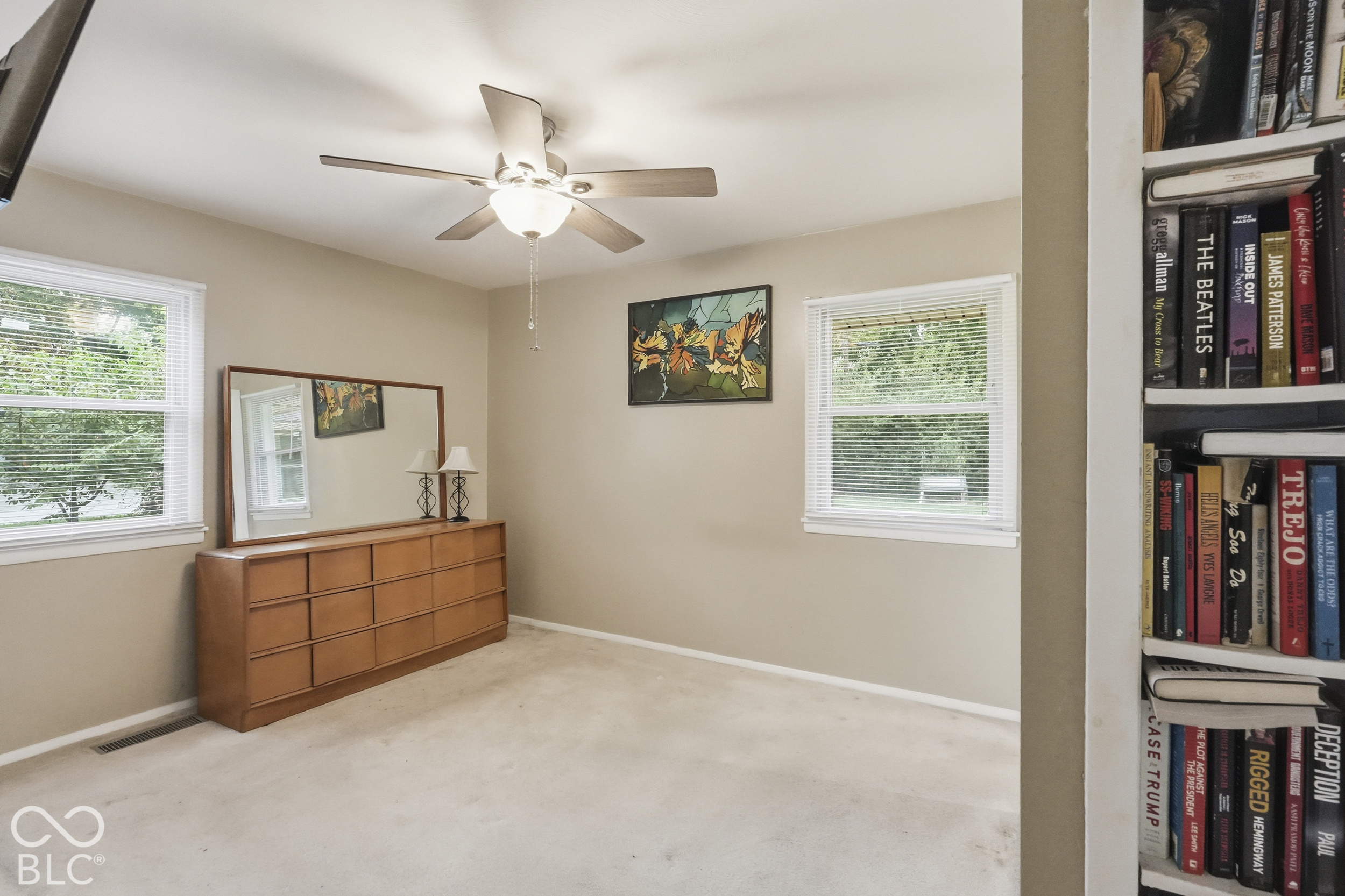 The primary suite has dual windows with white frames, a ceiling-mounted fan with integrated light fixture, and built-in shelving. The floor is carpeted.