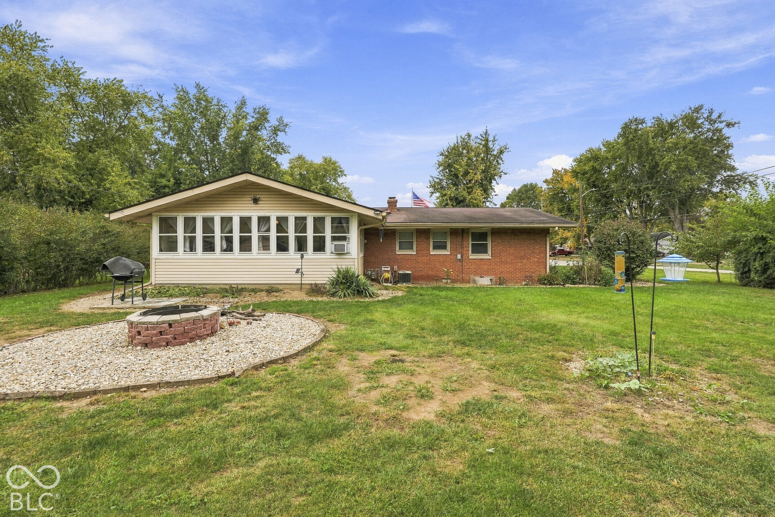 Rear exterior featuring the brick and siding facade, the sunroom with large windows, and the gravel fire pit.