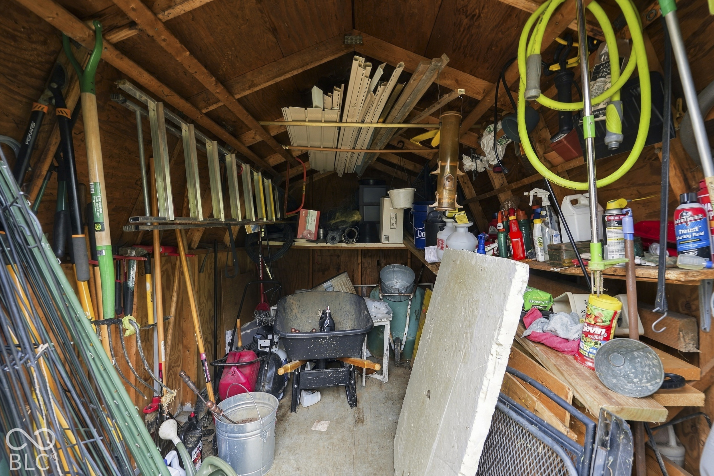 The storage shed with exposed wood framing, built-in shelving, and concrete flooring will store all of your yard care equipment throughout the year.