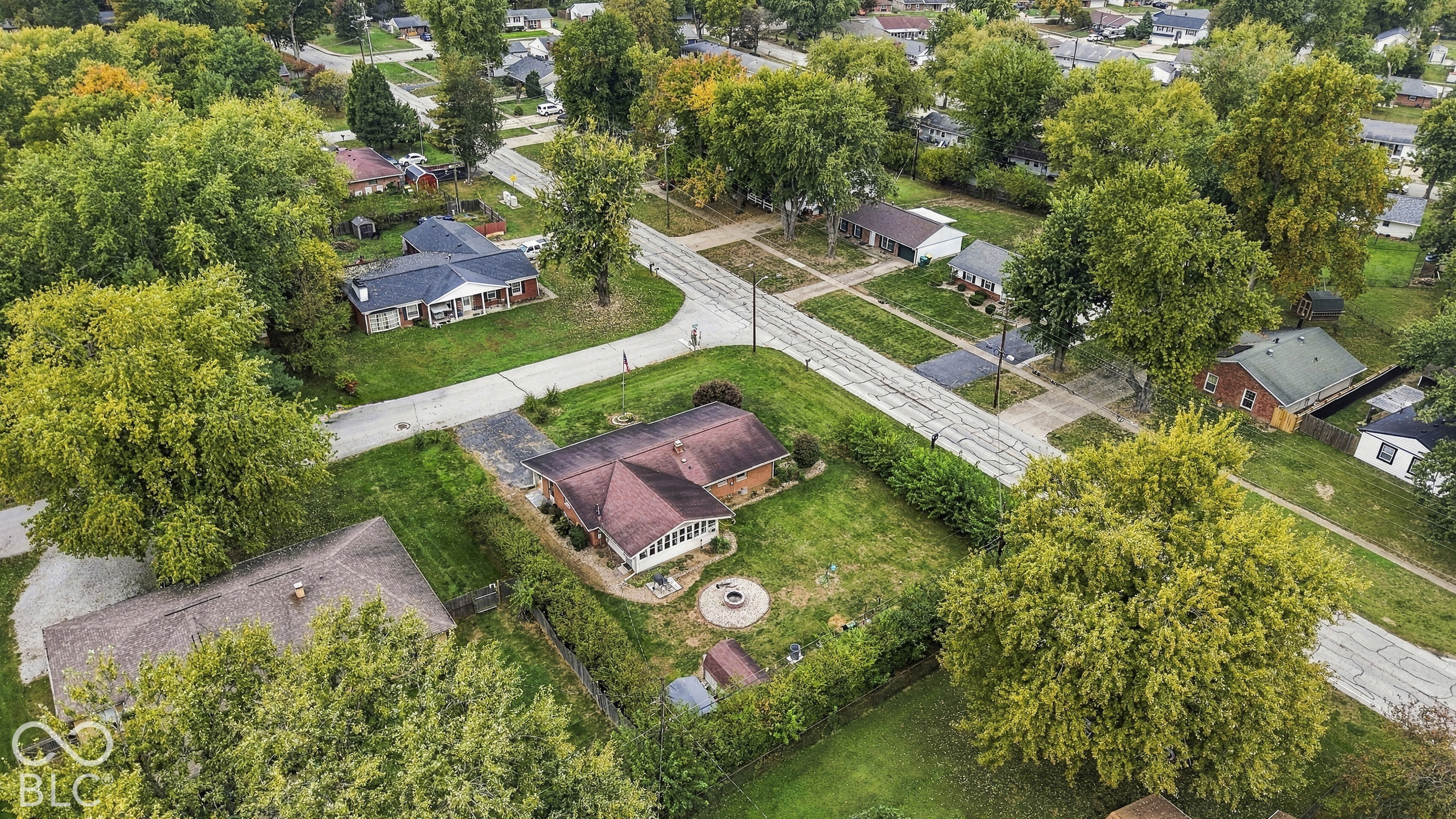 Aerial perspective of the detached single-story home situated on a corner lot, featuring mature trees, and a concrete driveway