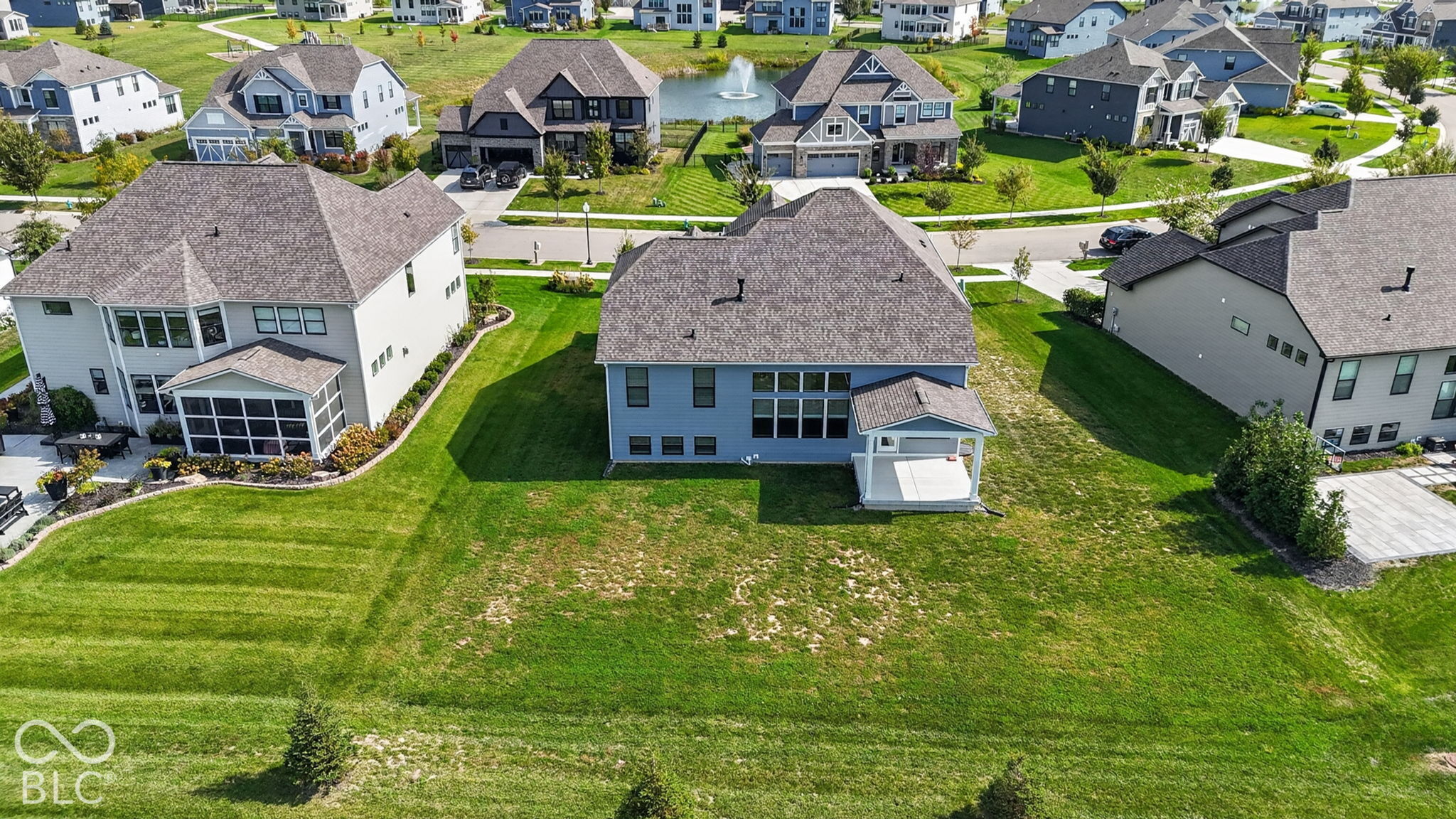 Aerial perspective of a multi-story residence featuring a covered rear patio, expansive lawn, stone-surfaced roof, and multi-pane windows