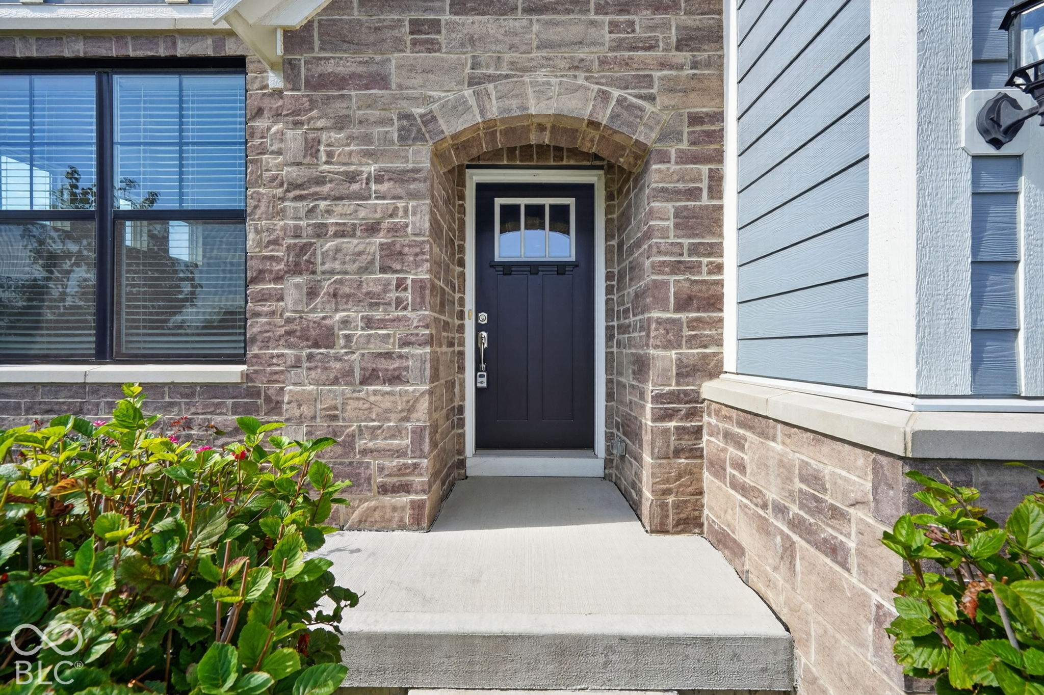 Exterior entryway featuring an arched stone facade, dark-toned front door with a transom light, lap siding, and a concrete porch