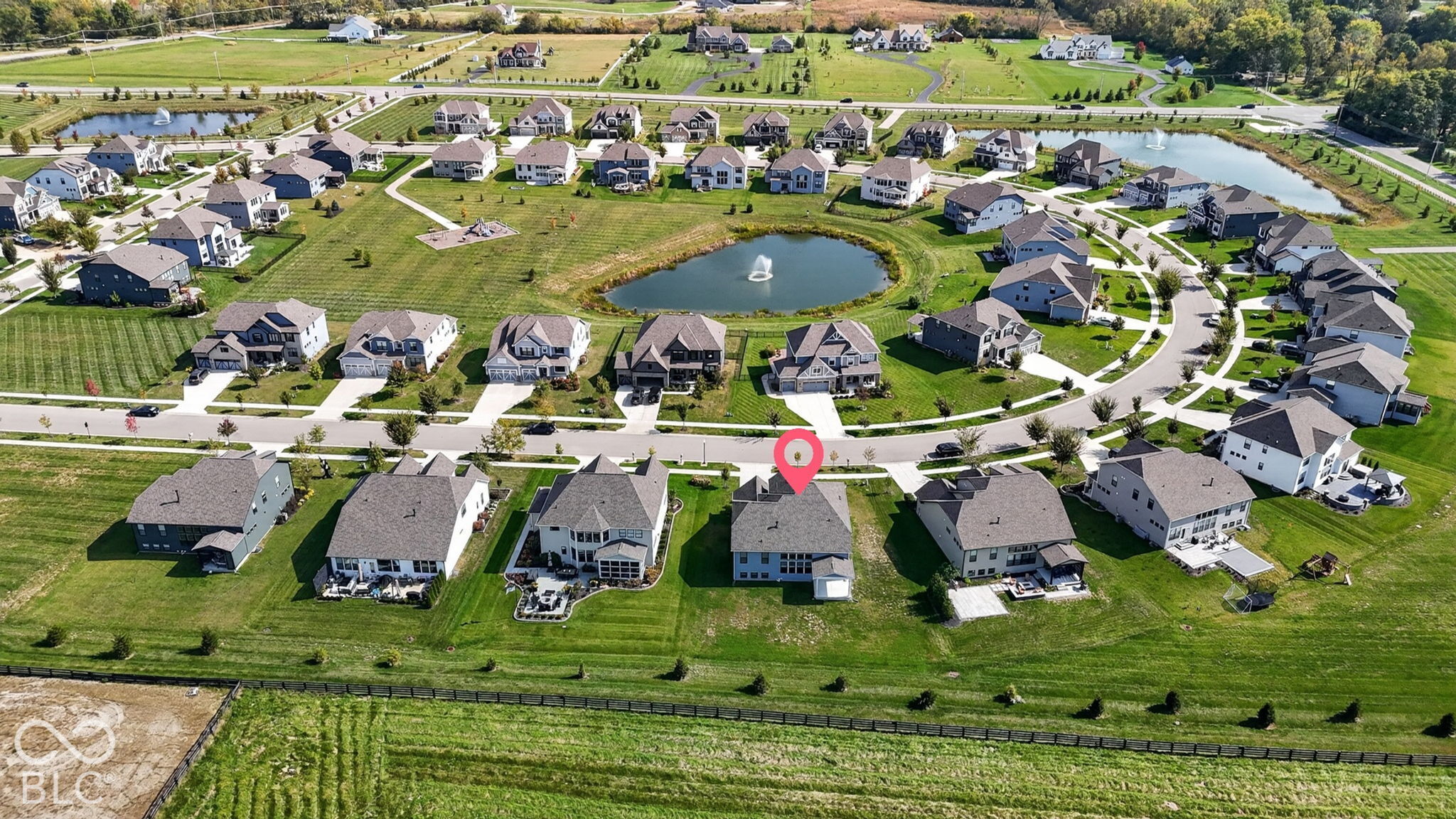 Aerial perspective of a residential community featuring a central pond with a fountain, paved cul-de-sac streets, manicured green spaces, and dense perimeter landscaping