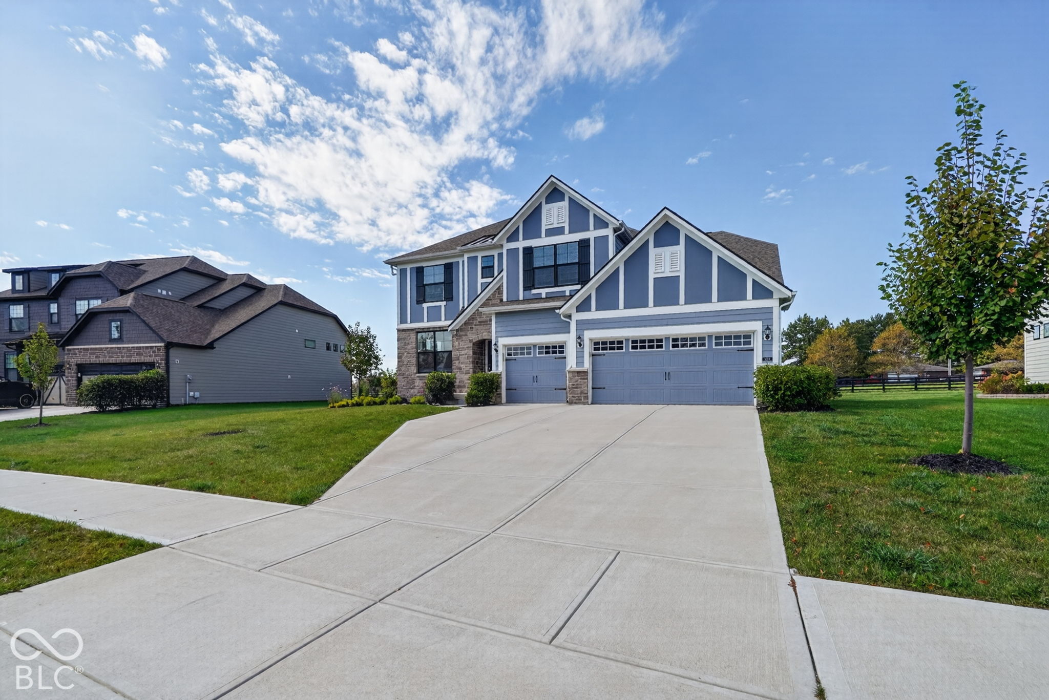 Two-story residence featuring blue horizontal siding with white trim, stone veneer accents, a three-car garage, and a concrete driveway