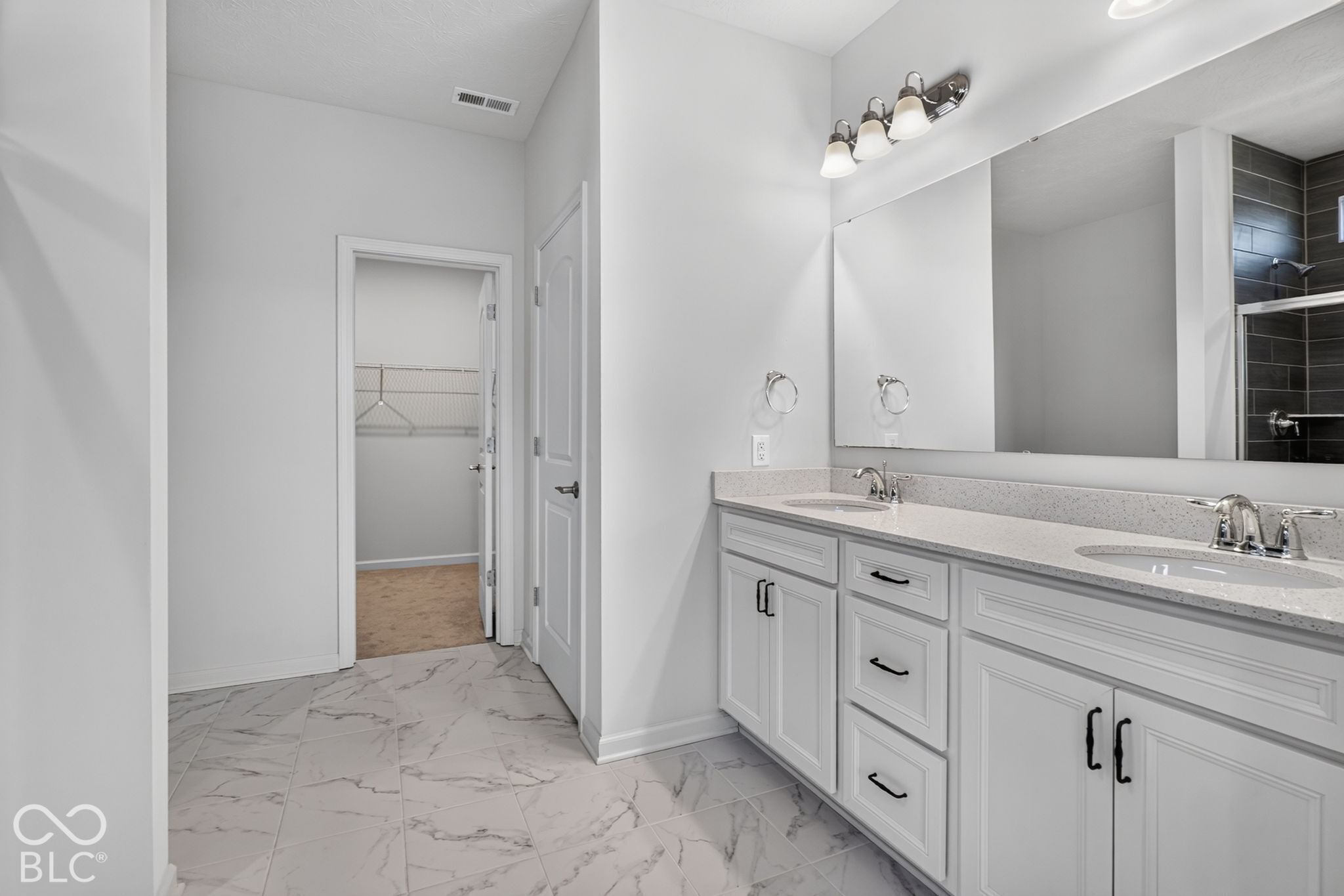 Bathroom featuring a dual-sink vanity with white cabinetry, stone-finish countertops, large vanity mirror, and marble-patterned tile flooring