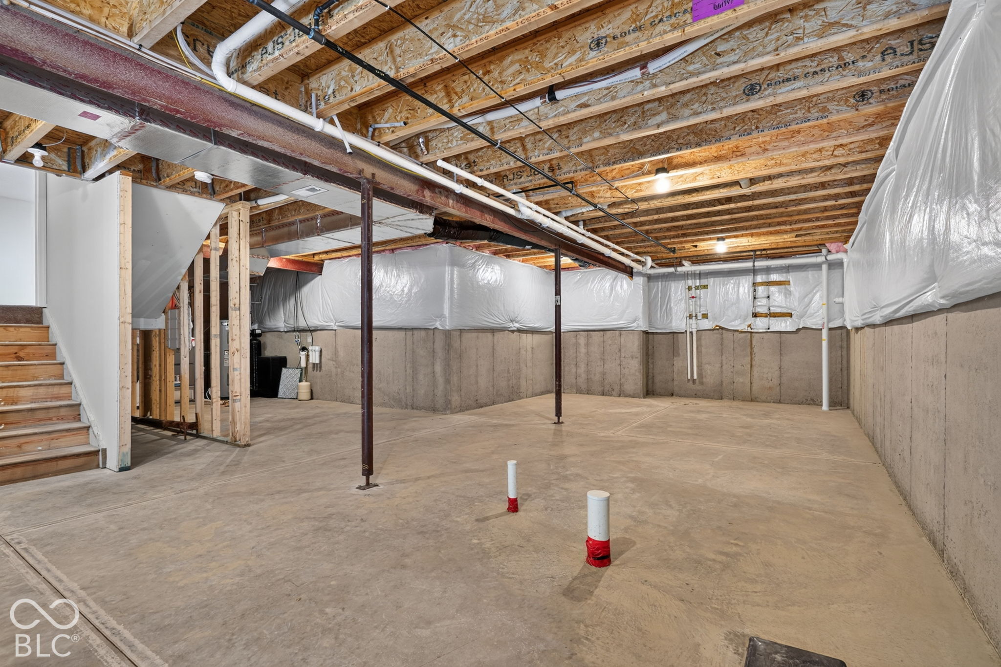 Unfinished lower level featuring poured concrete walls, exposed wood ceiling joists, concrete flooring, and structural steel support columns