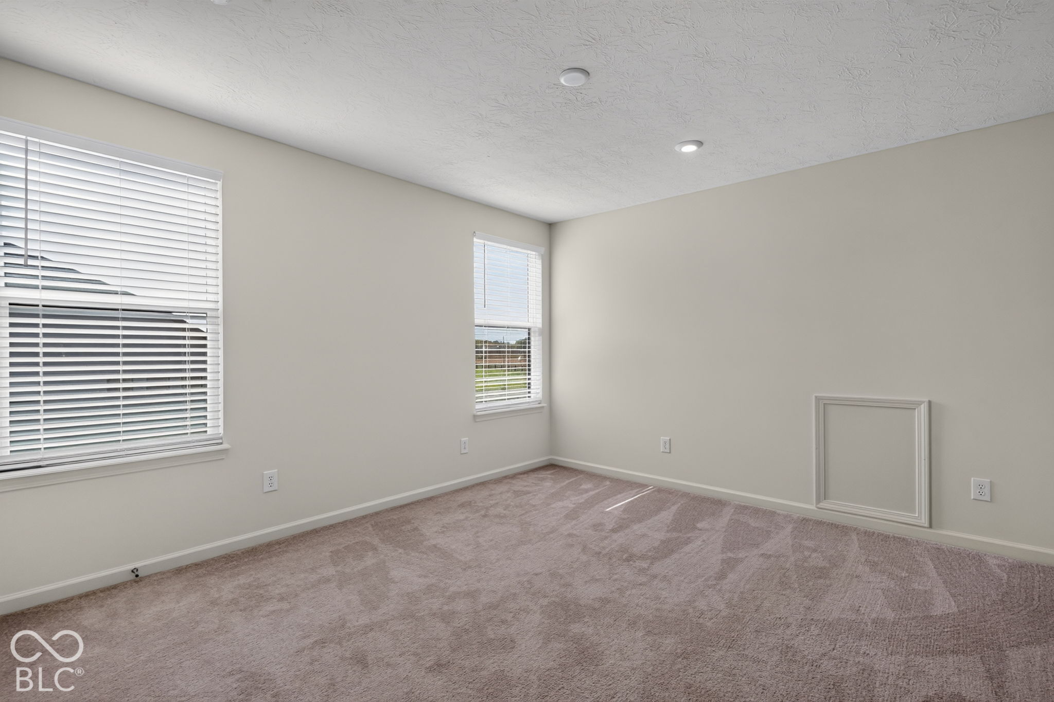 Neutral-toned interior space featuring wall-to-wall carpeting, recessed ceiling lighting, and dual windows with fitted horizontal blinds