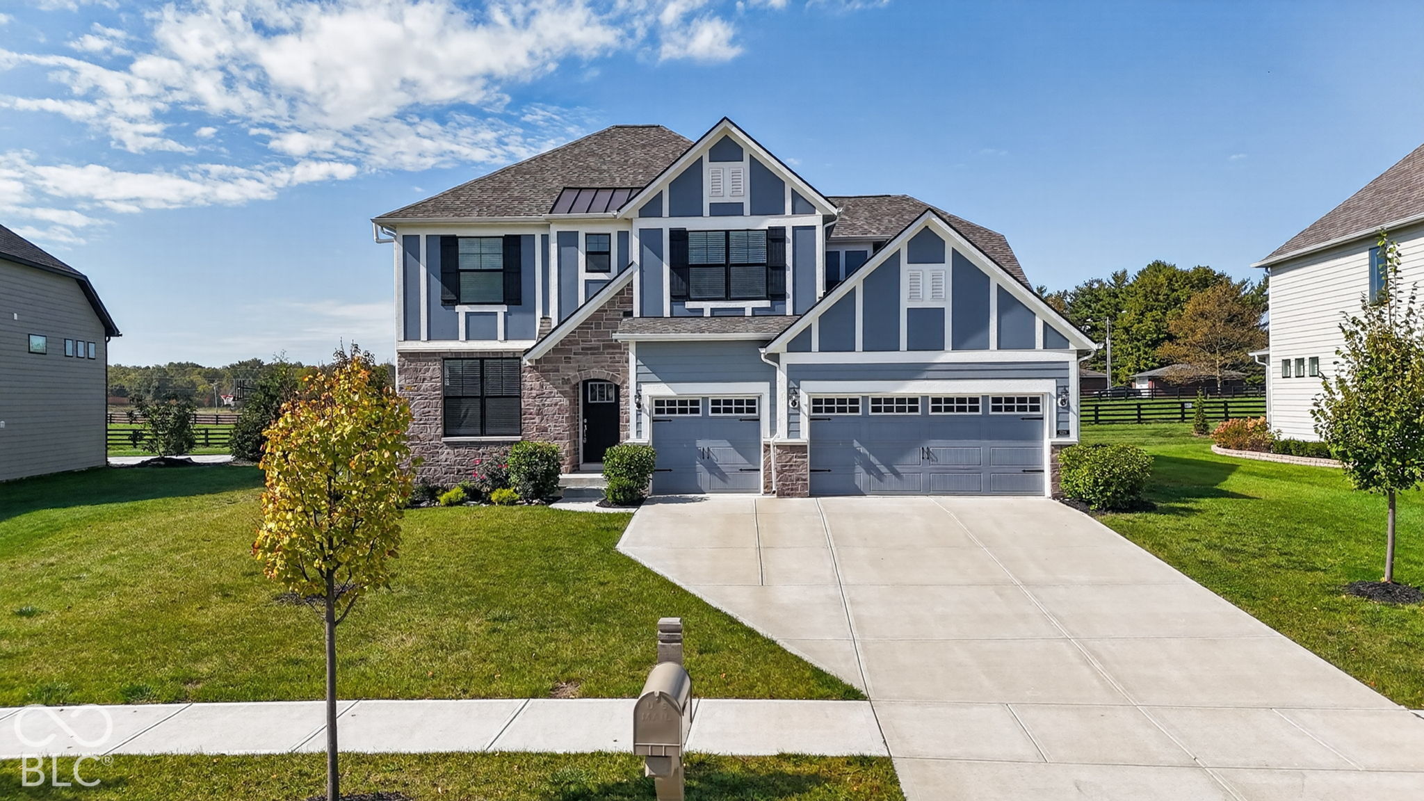 Two-story exterior featuring stone veneer and vertical siding, multi-gabled roofline, three-car garage, and concrete driveway