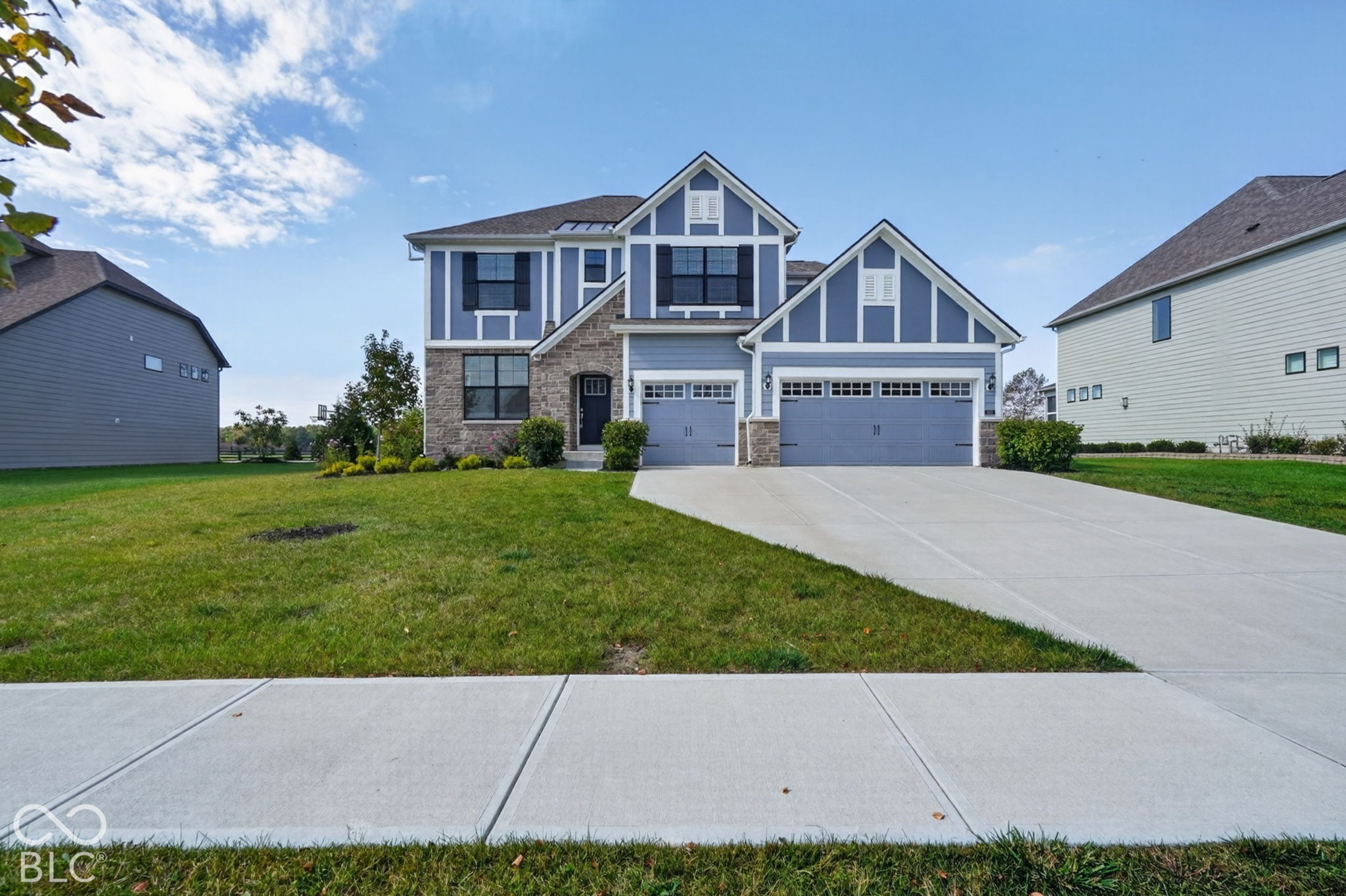 Two-story exterior featuring board and batten siding, stone veneer accents, a three-car garage, and a concrete driveway