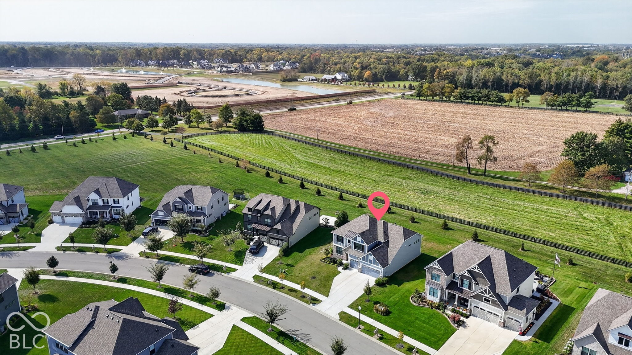 Aerial perspective featuring a two-story residence with a multi-gabled roof, attached garage, concrete driveway, and a backyard bordered by fenced pastureland