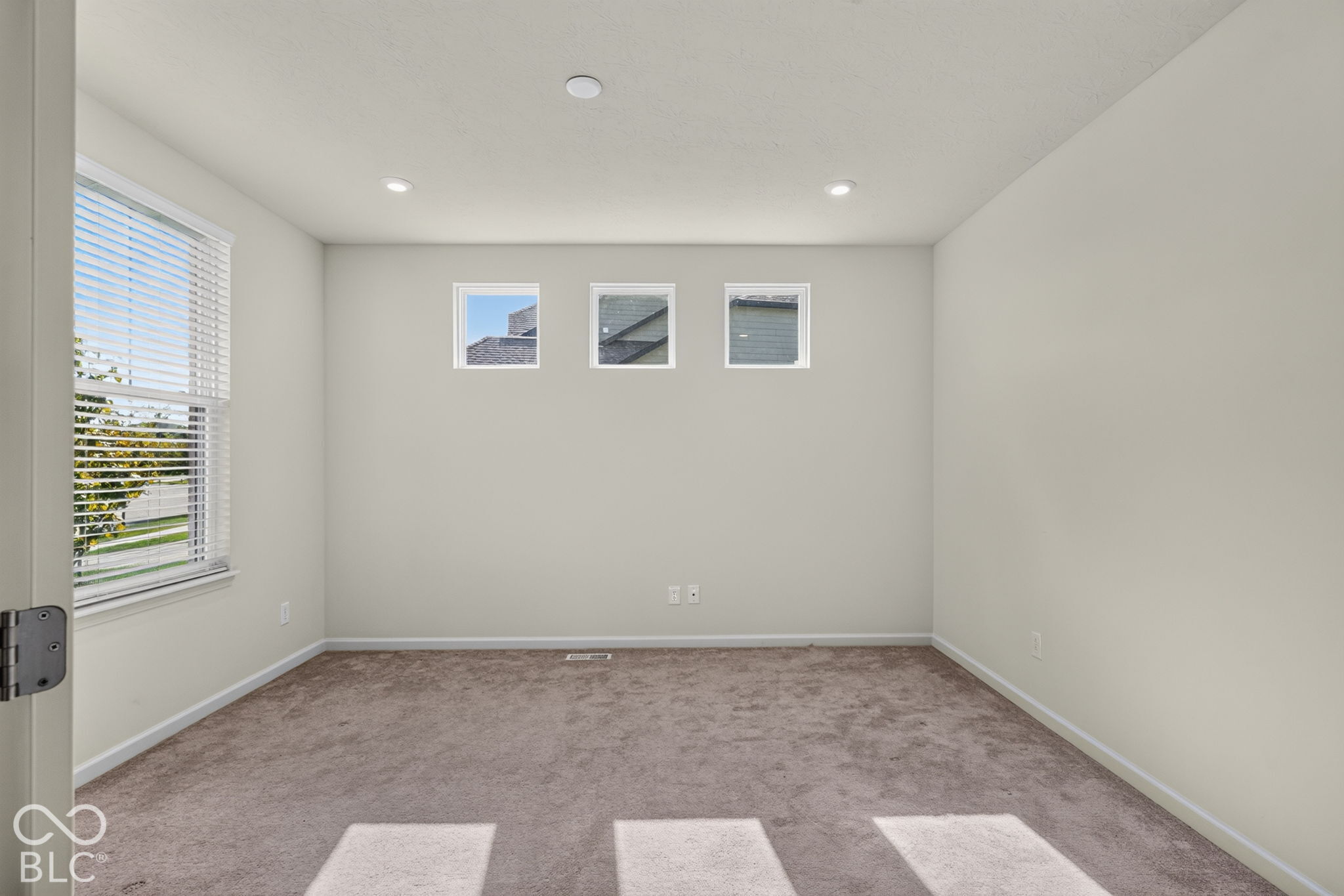 Interior space featuring neutral-toned carpeting, high-positioned square accent windows, recessed lighting, and a large side-wall window with horizontal blinds