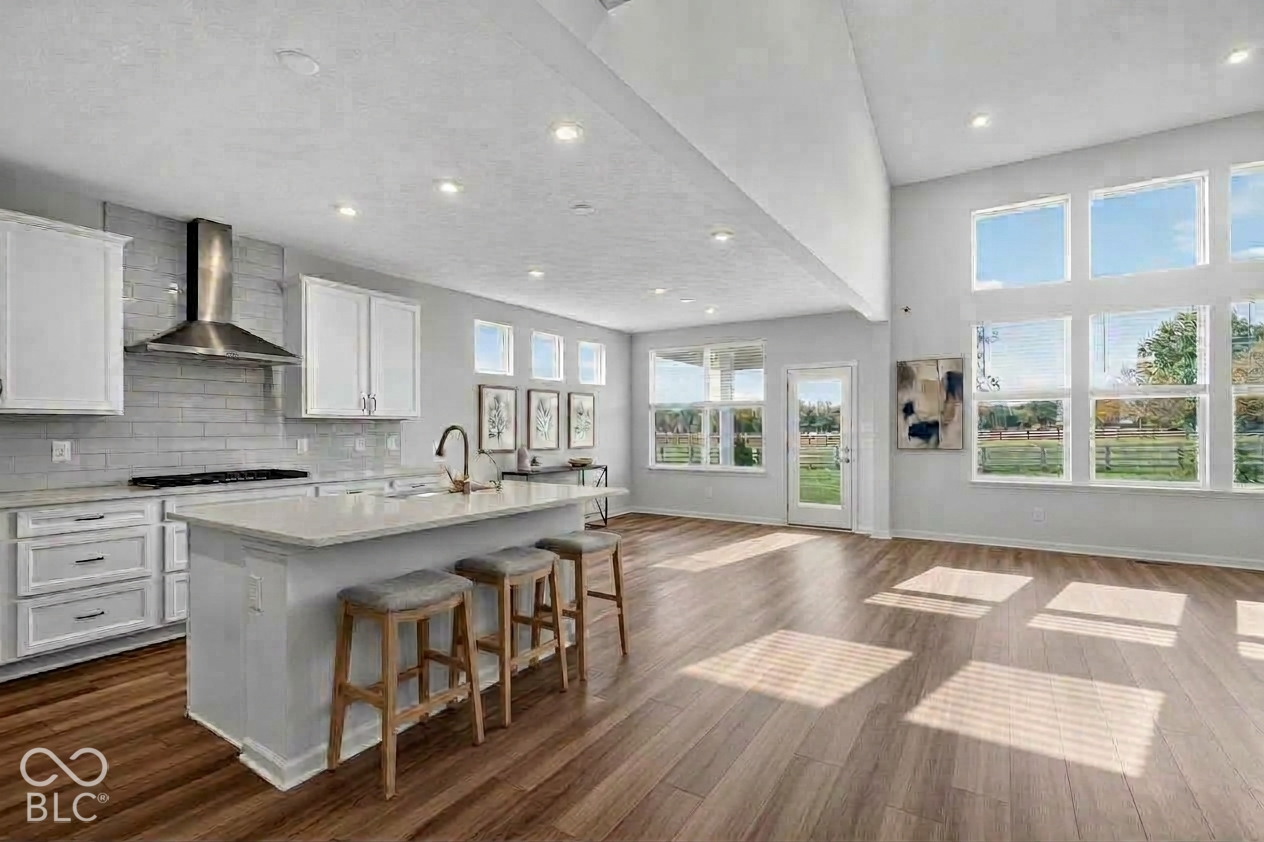Virtually Altered - Open-concept kitchen featuring an expansive center island, ceiling-height windows, stainless steel range hood, stone-finish backsplash, and wood-finish flooring