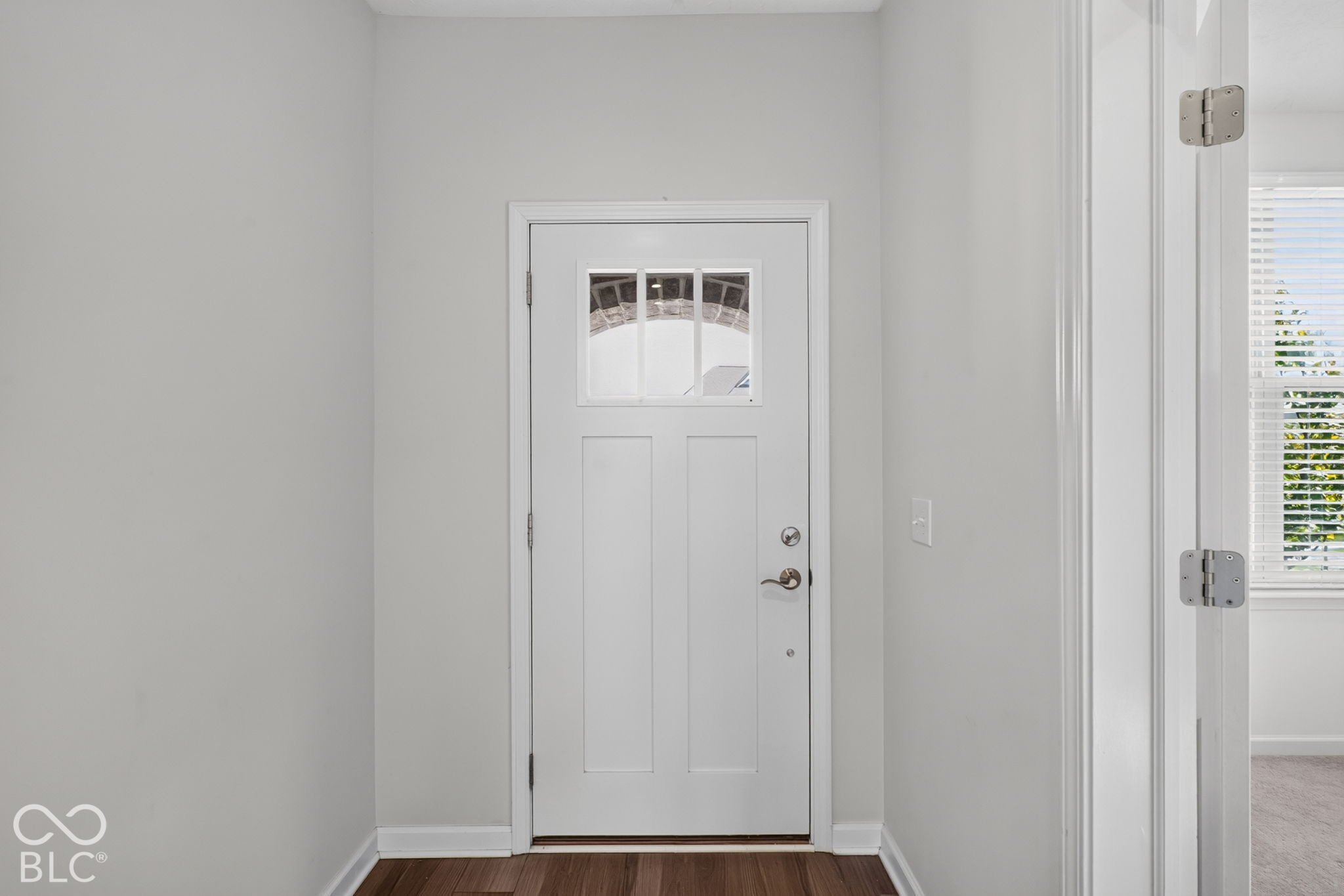 White entry door featuring a three-pane window insert, satin nickel hardware, and dark wood-finish flooring