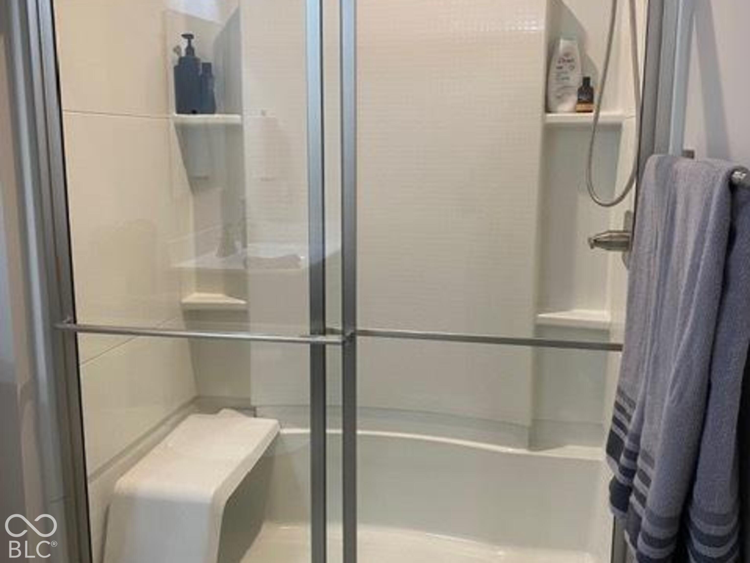 Shower enclosure featuring a built-in bench, sliding glass doors with brushed metal framing, integrated shelving, and a wall-mounted shower head