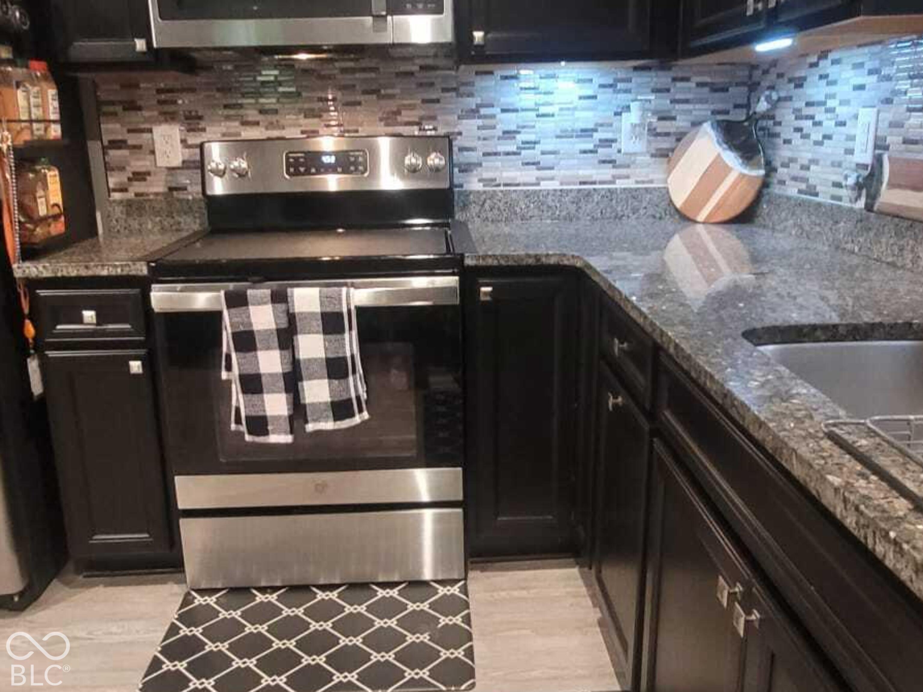 Kitchen featuring dark cabinetry, stainless steel appliances, stone-surface countertops, and a textured tile backsplash