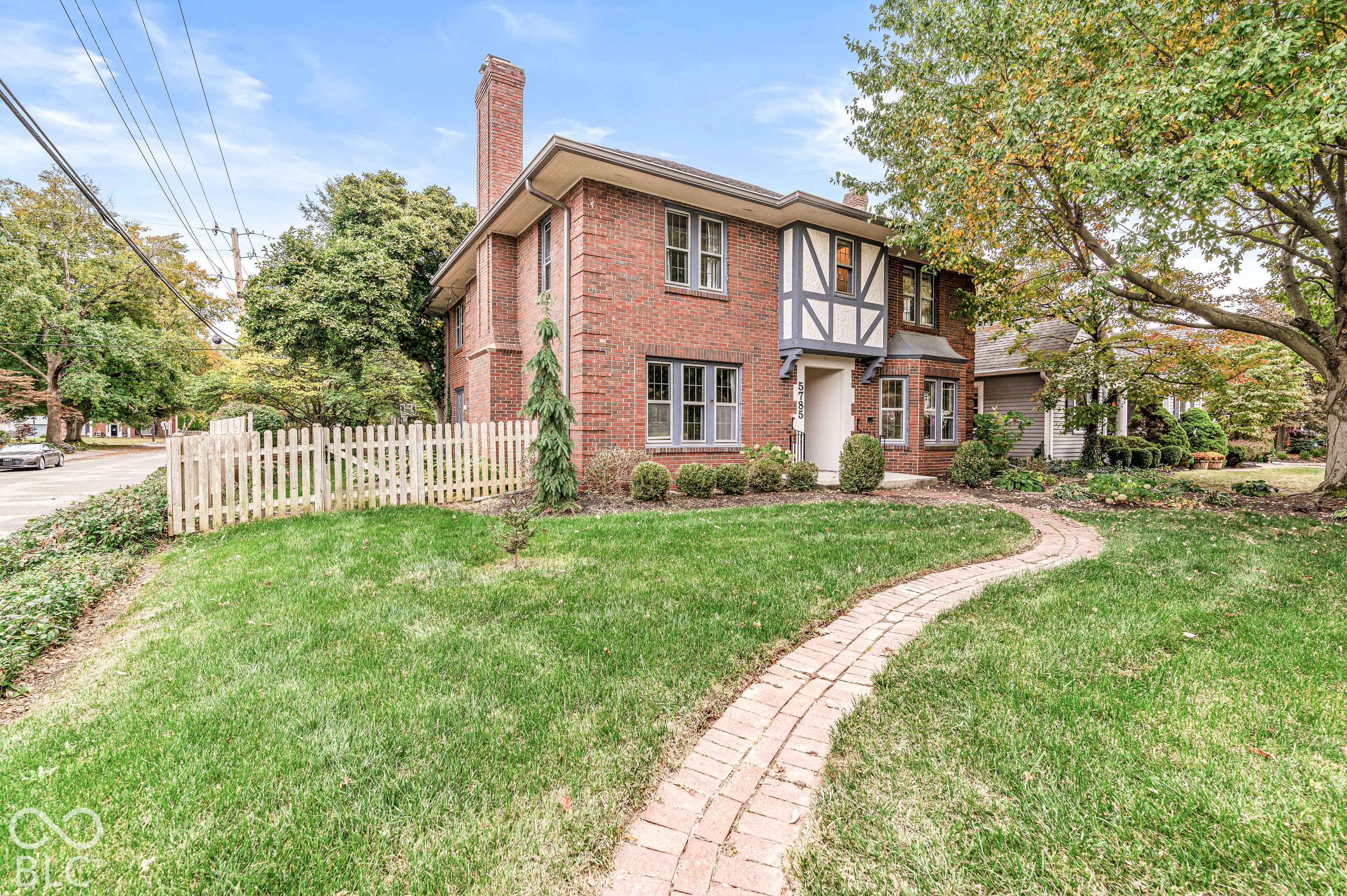 Traditional brick exterior featuring Tudor-style timber framing, a prominent chimney, multi-pane windows, and a paved brick pathway