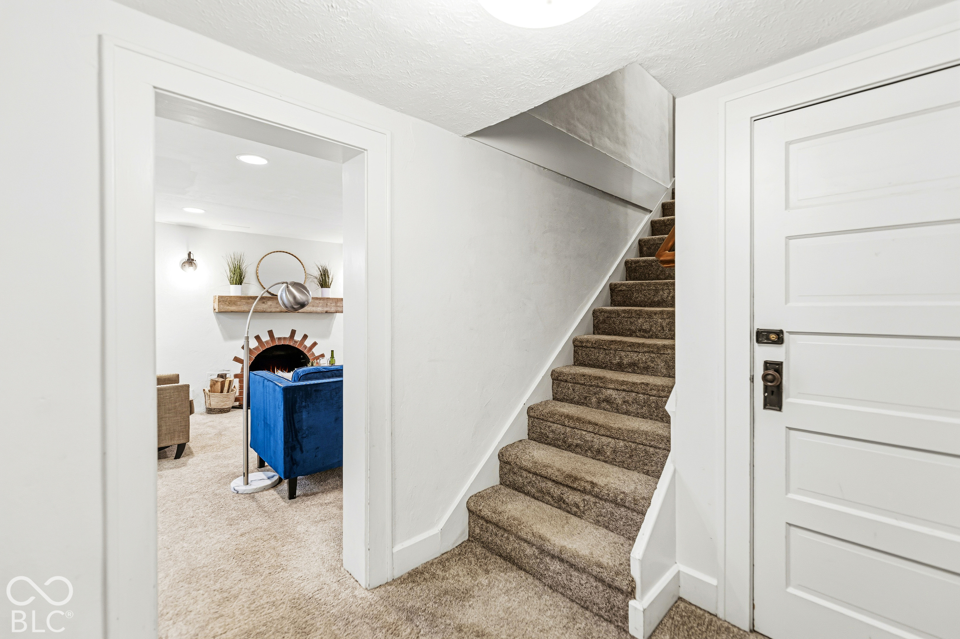 Carpeted staircase with white trim, five-panel interior door, and arched brick fireplace surround with a wooden mantel