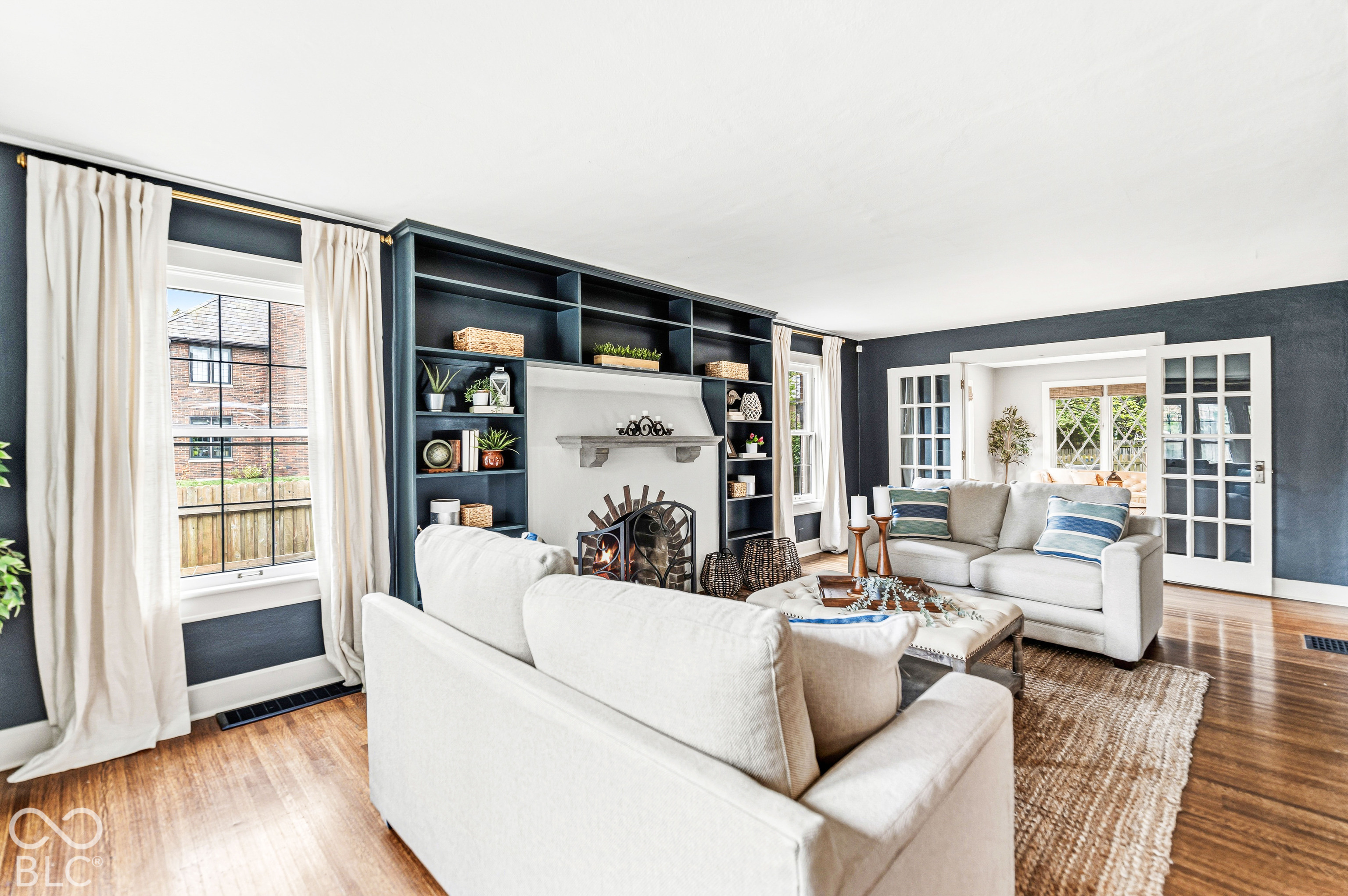 Living space featuring hardwood flooring, a masonry fireplace with a stone mantel, floor-to-ceiling built-in shelving, and white-paned French doors