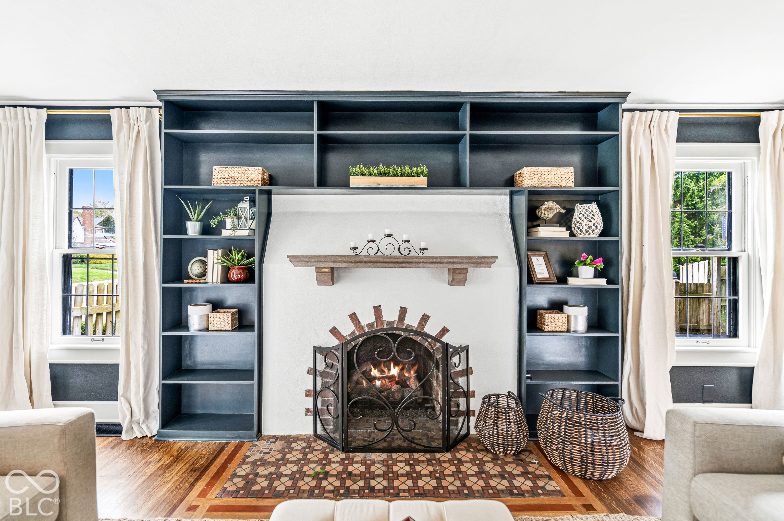 Floor-to-ceiling dark-toned built-in shelving, central fireplace with arched brick detailing, wood-finish flooring with decorative inlay, and wood mantel