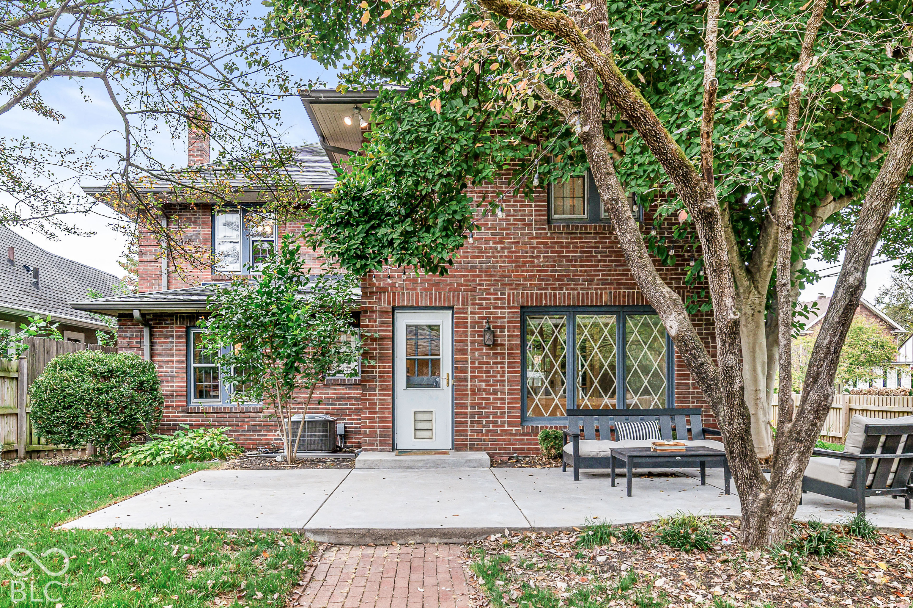 Brick exterior with concrete patio, lattice-style window detailing, and mature landscaping