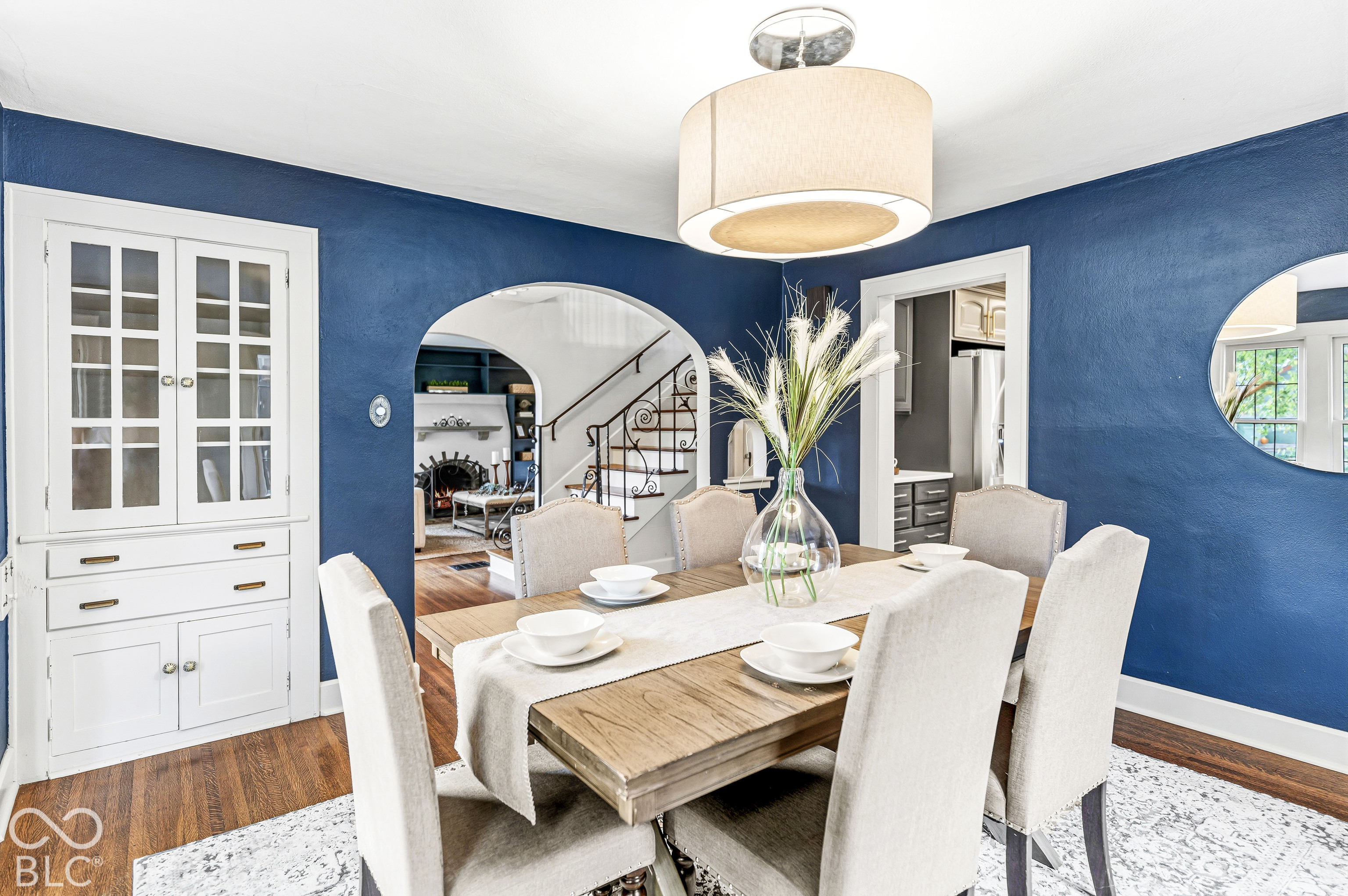 Built-in white hutch with glass-front cabinetry, drum pendant lighting, arched entryway, wood-finish flooring, and circular wall mirror