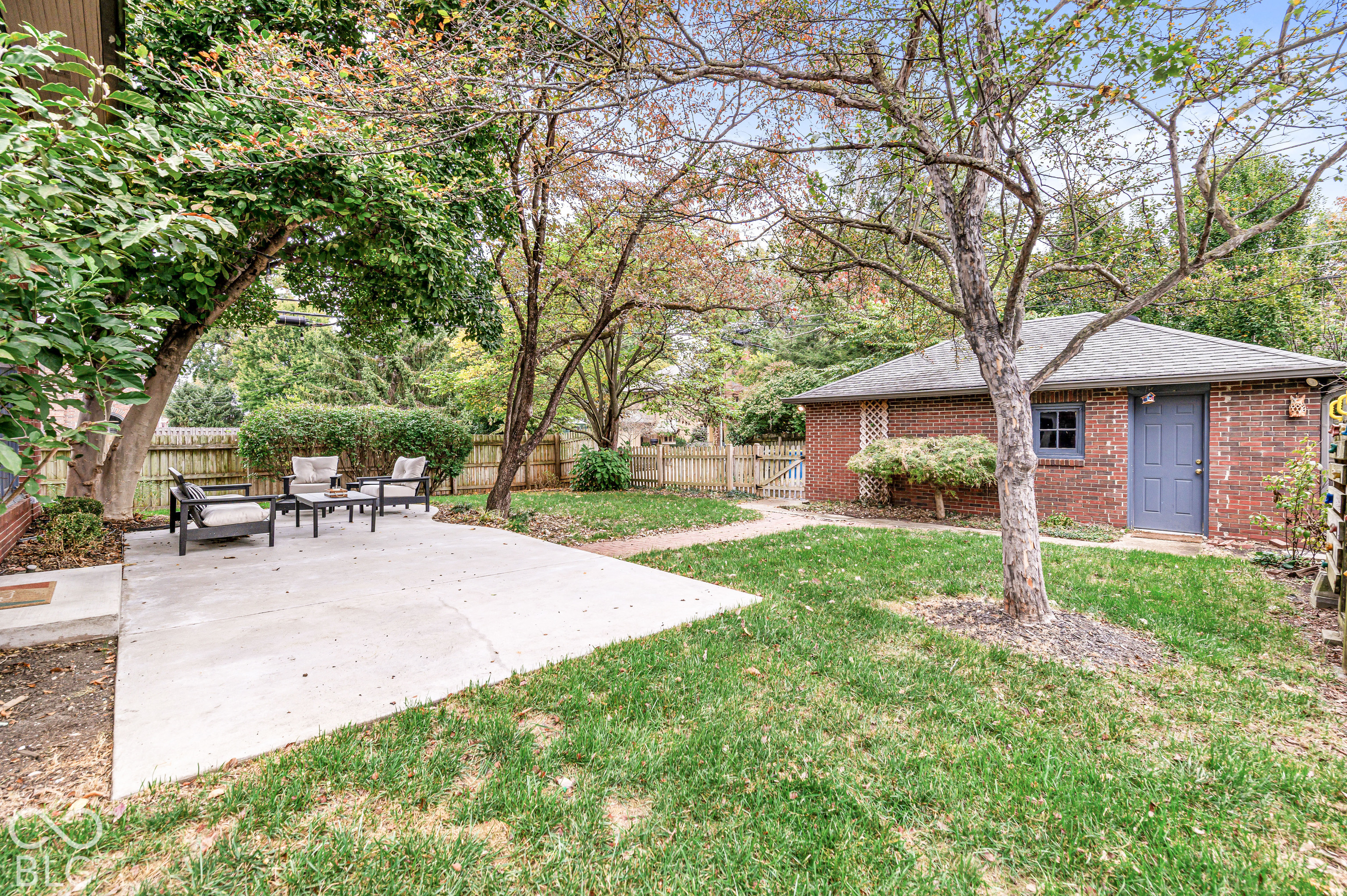 Private backyard featuring a concrete patio, brick detached garage, mature trees, and wood-fence perimeter