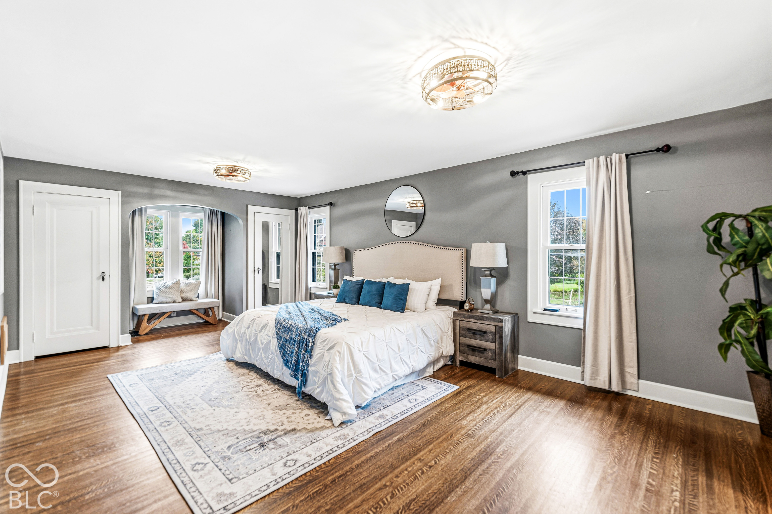 Room featuring wood-finish flooring, recessed arched window nook, and dual multi-tier flush mount light fixtures