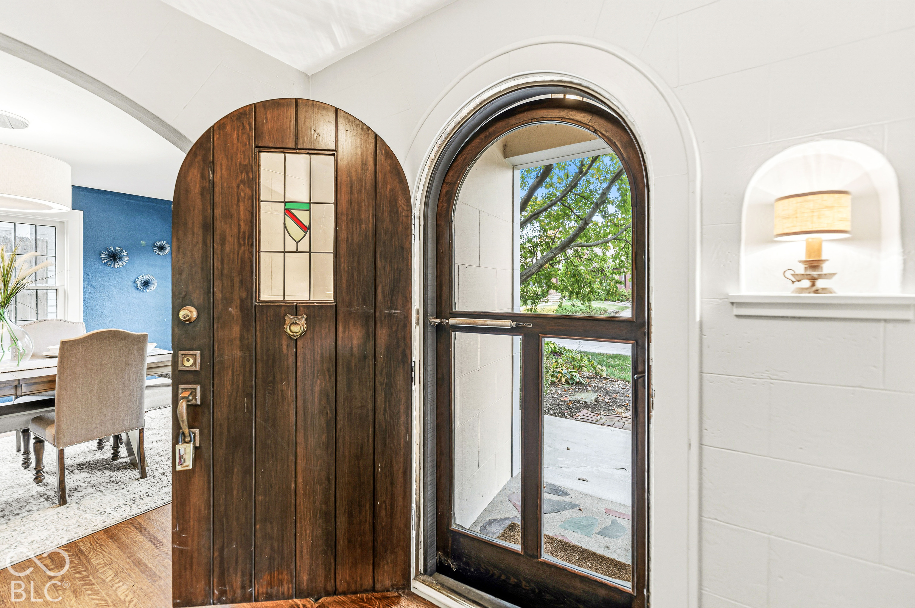 Arched wooden entry door featuring a stained-glass inset, stone-textured threshold, and a recessed wall niche with built-in shelving