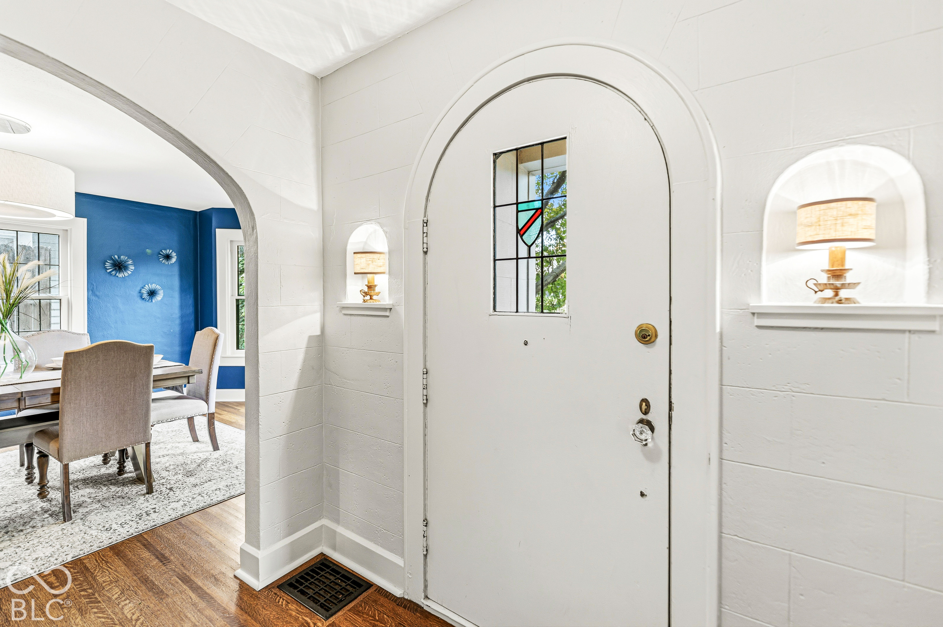 Arched doorway featuring a solid door with an inset stained-glass pane, recessed wall niches, and wood-finish flooring