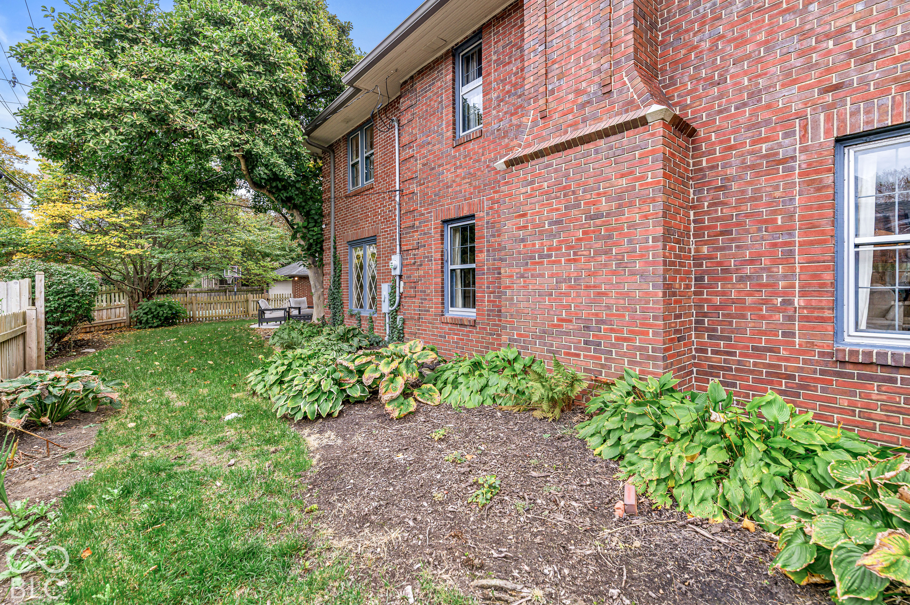 Red brick exterior featuring decorative leaded glass window detailing, mature landscape plantings, and a fenced yard