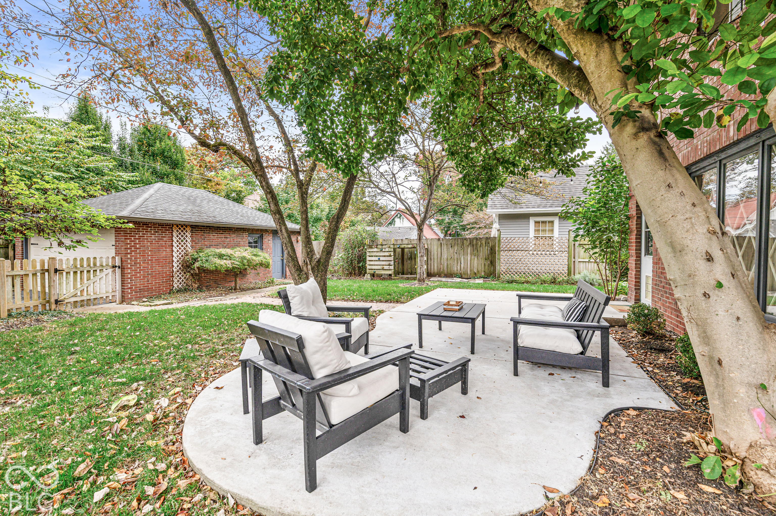 Backyard featuring a concrete patio, red brick exterior wall, detached brick garage, mature trees, and wooden perimeter fencing