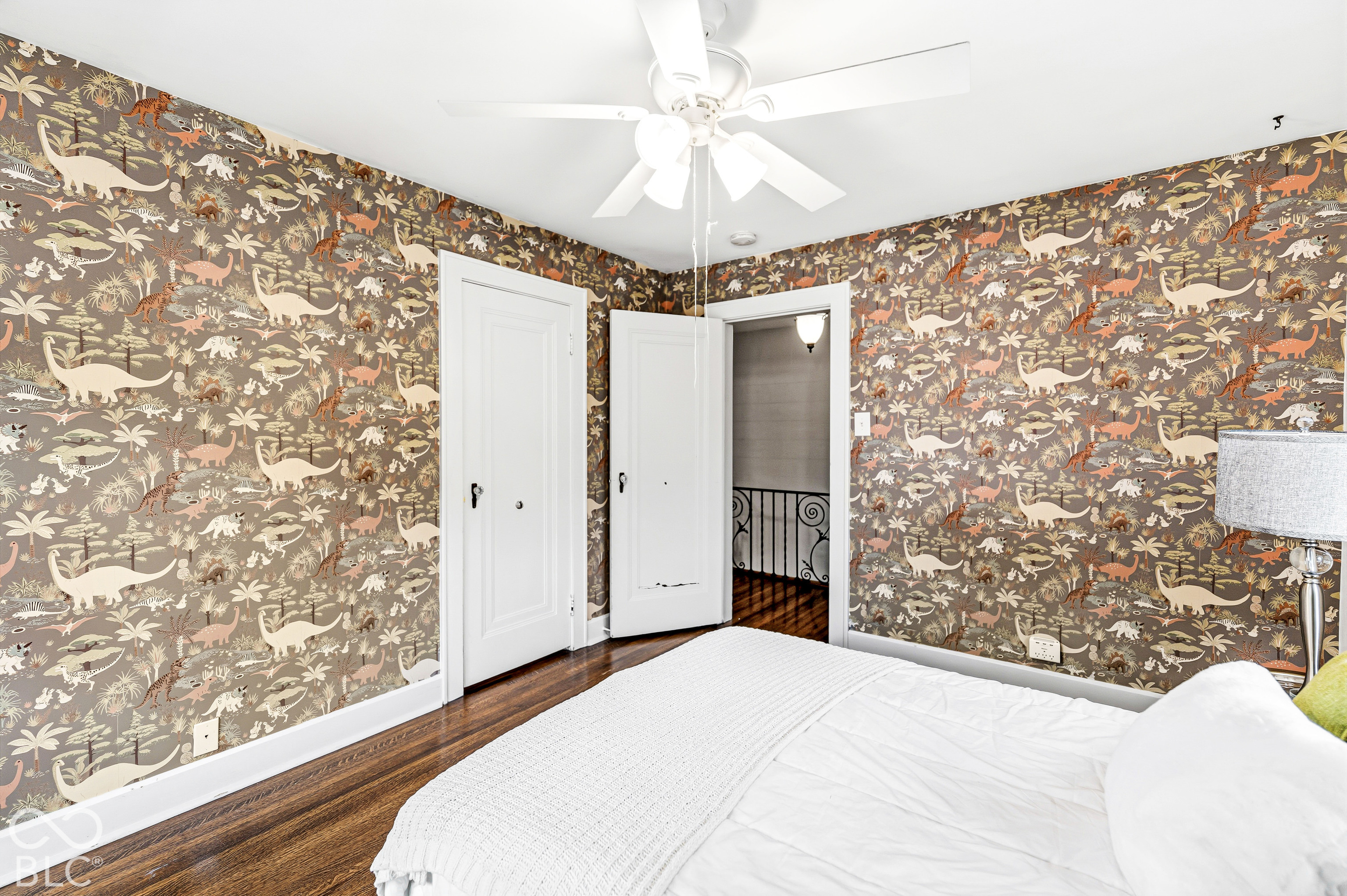Room featuring patterned wallpaper, dark-toned wood-finish flooring, a white ceiling fan with multi-light fixture, and two-panel interior doors