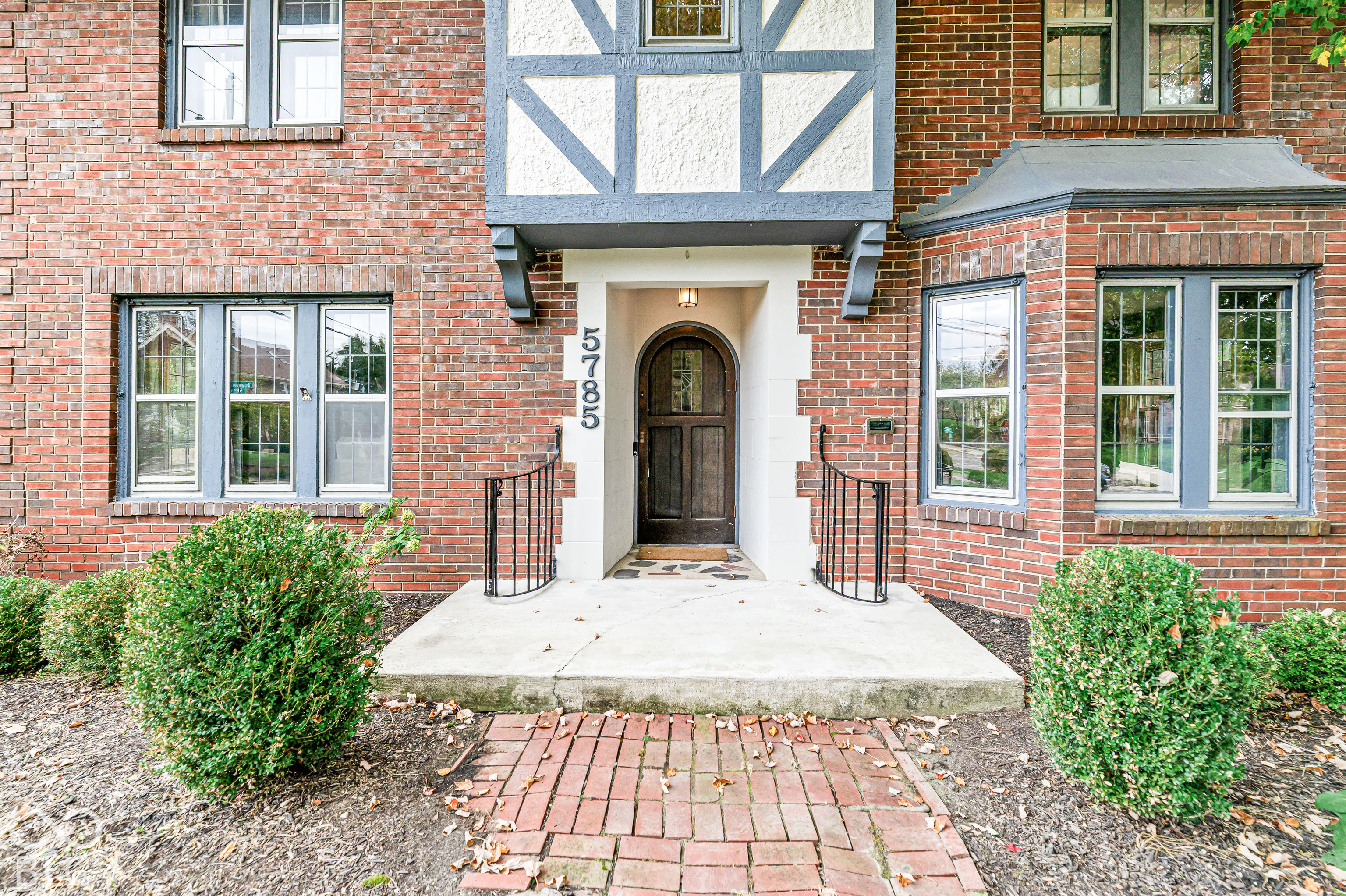 Tudor-style exterior featuring red brick masonry, decorative timber-framing accents, a curved wood-panel entry door, and a brick-paved walkway