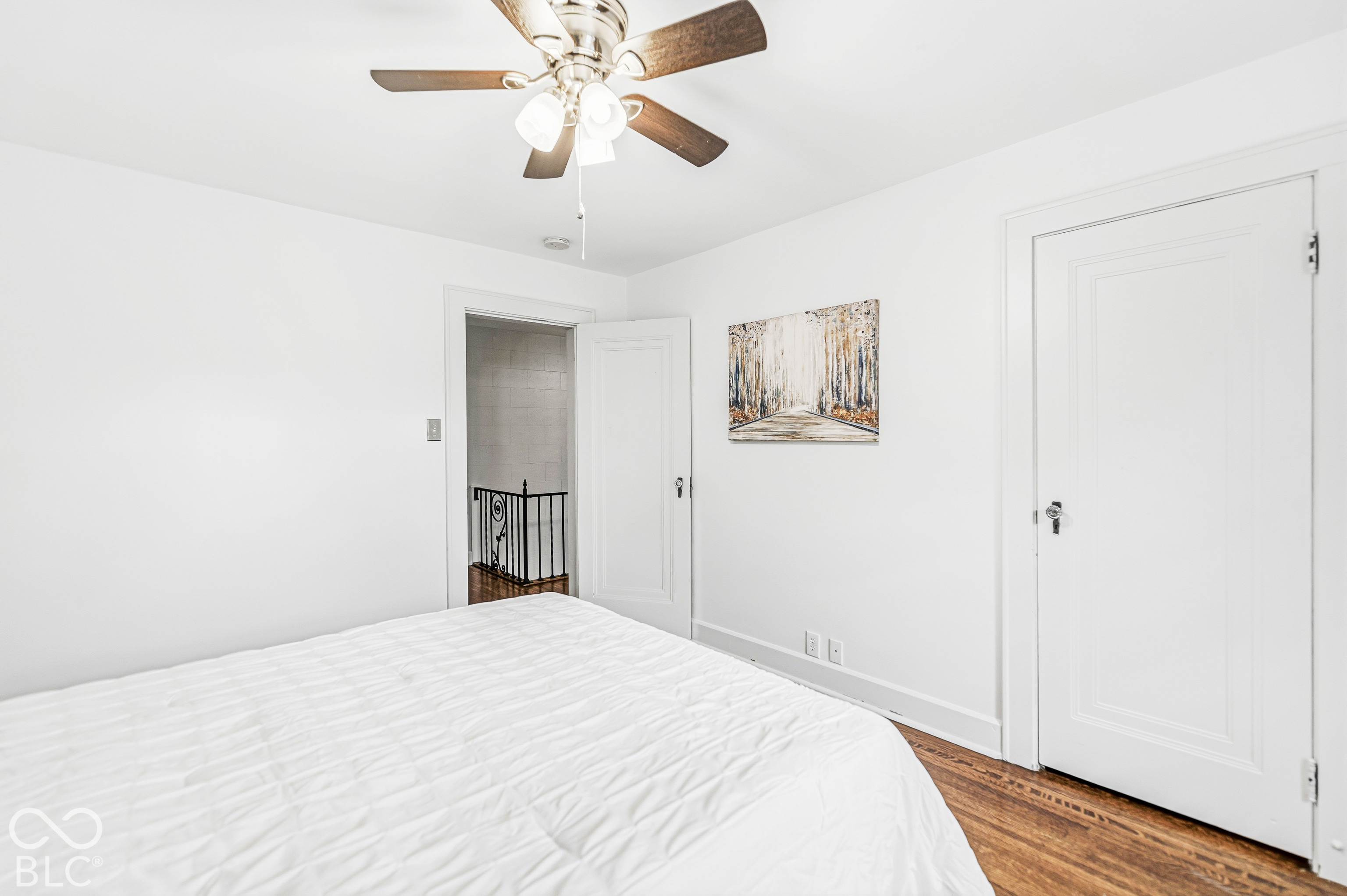 Room featuring wood-finish flooring, a multi-blade ceiling fan with integrated lighting, and solid-core interior doors with hardware