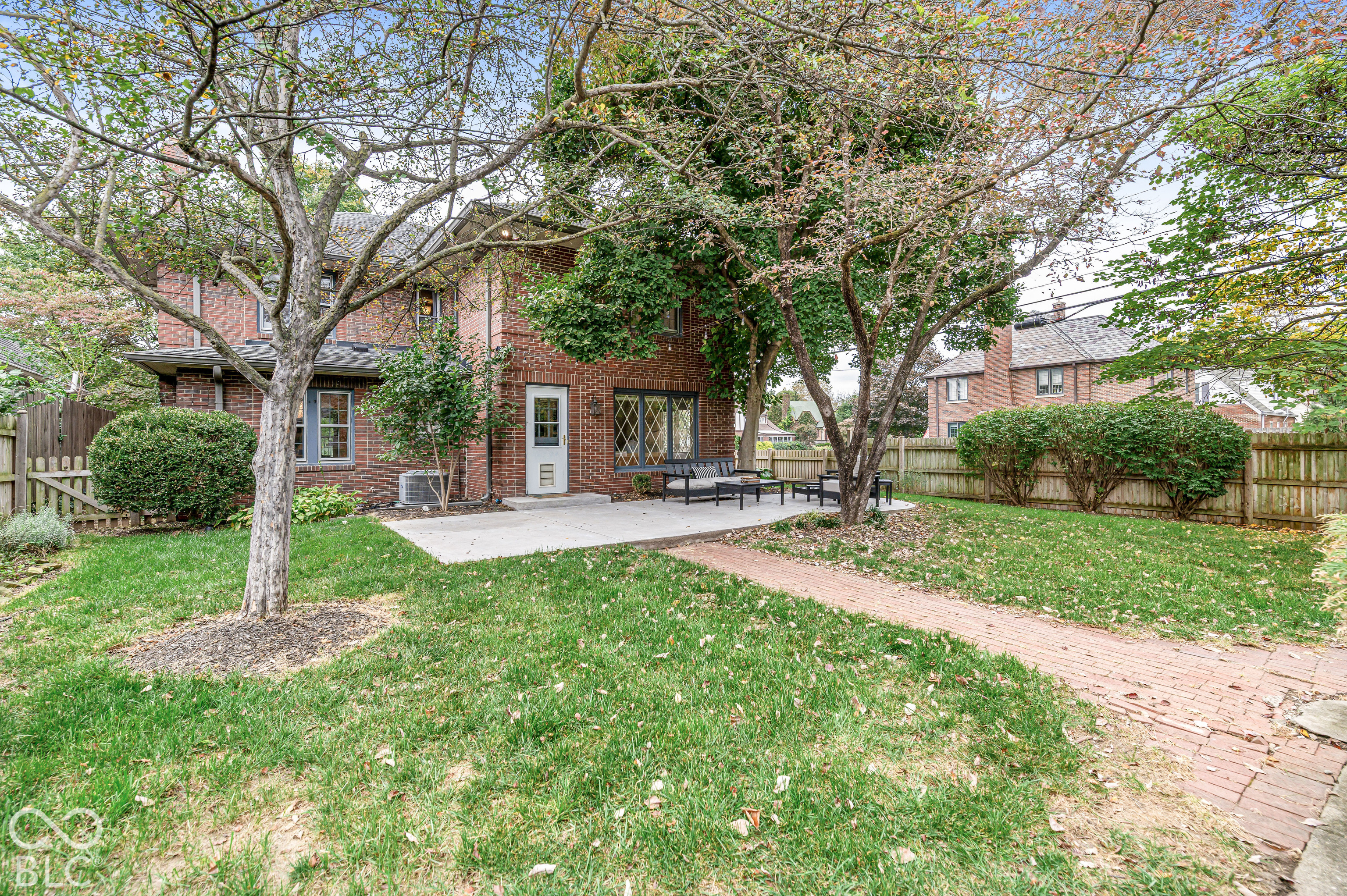Brick exterior featuring a concrete patio, a brick paver walkway, mature trees, and wooden privacy fencing