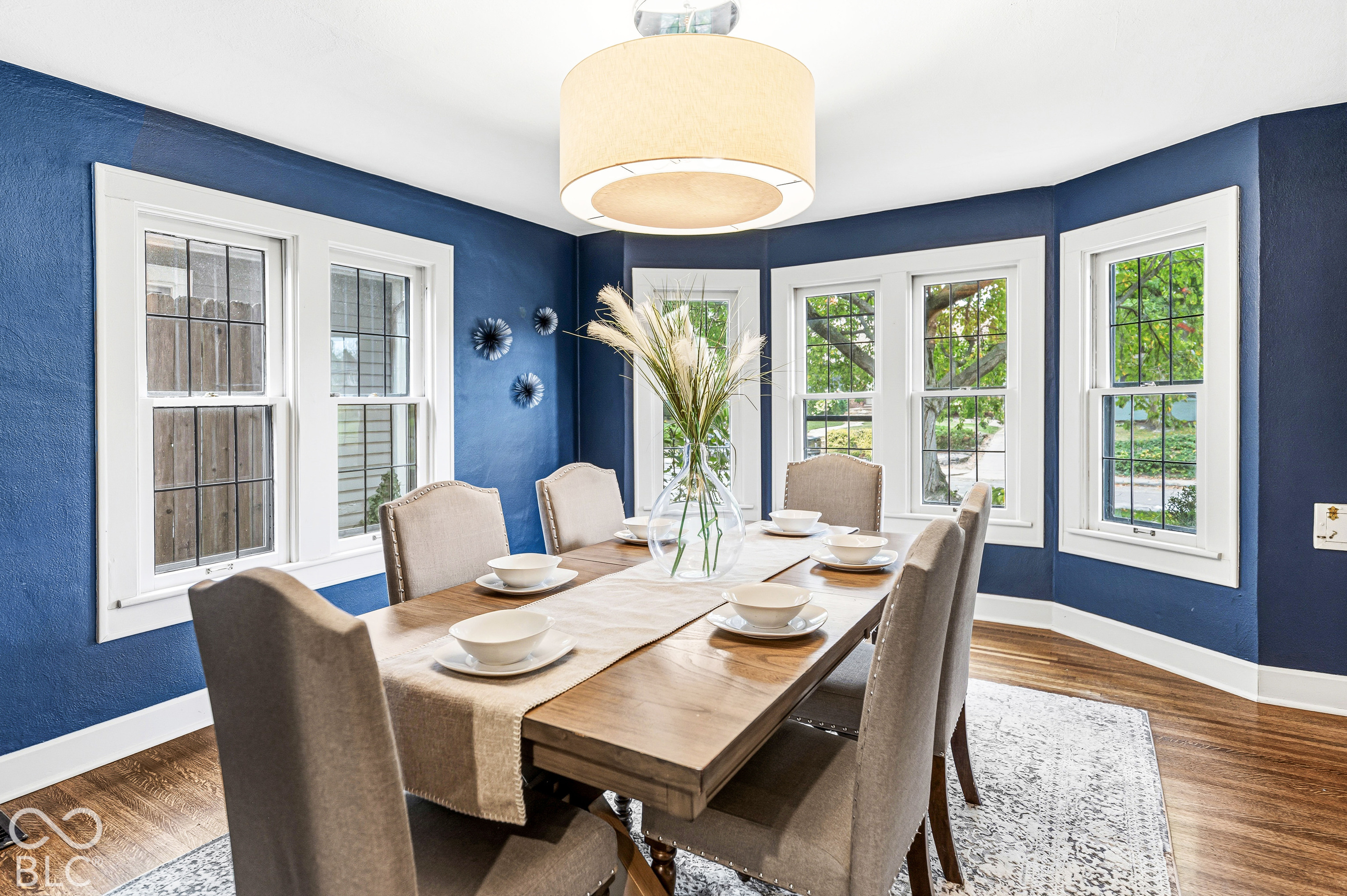 Dining area featuring wood-finish flooring, a multi-window bay configuration, white millwork trim, and a drum-style pendant light fixture