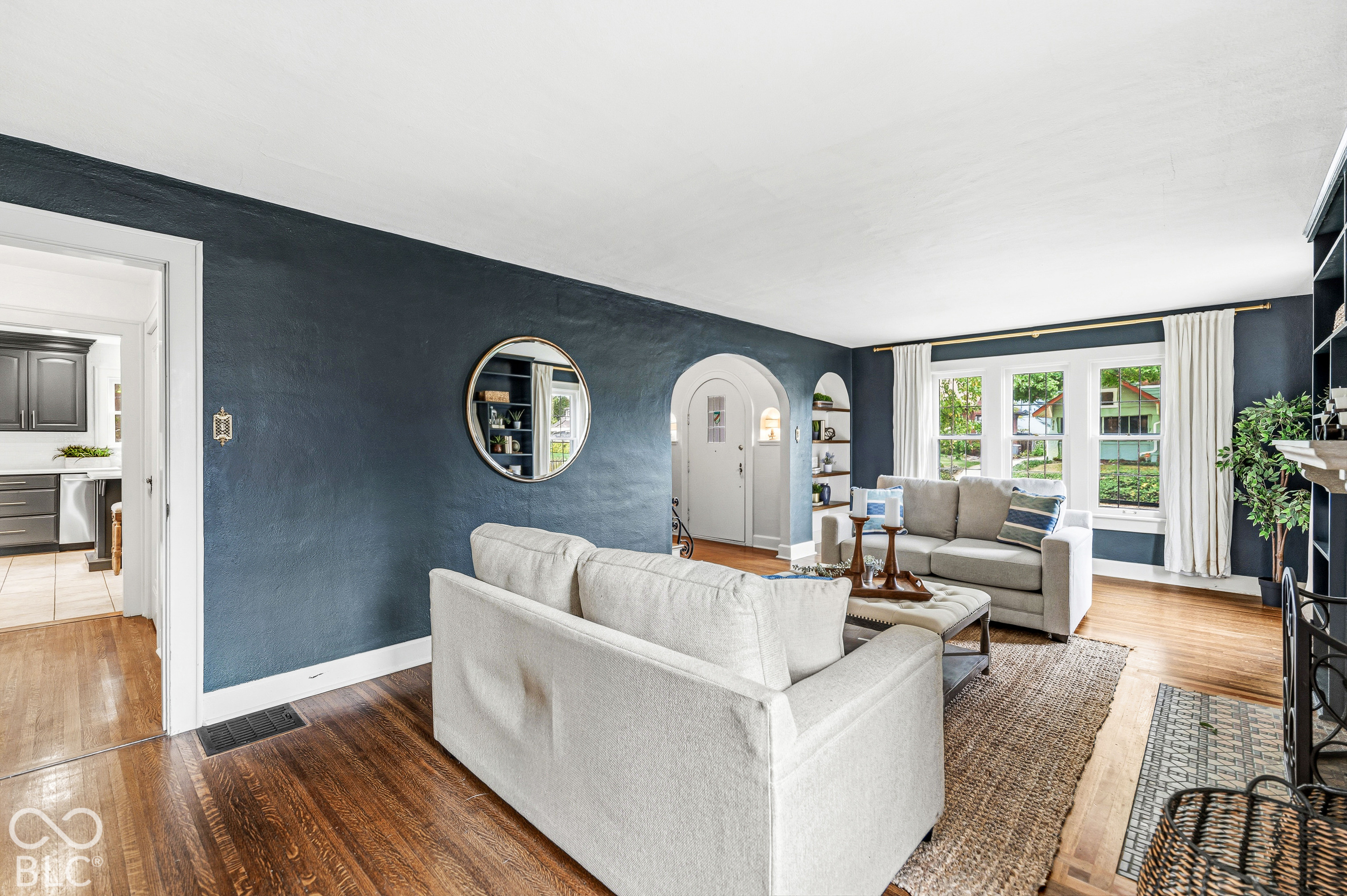 Living area featuring wood-finish flooring, textured navy walls, arched architectural detailing, built-in shelving, and multipane windows