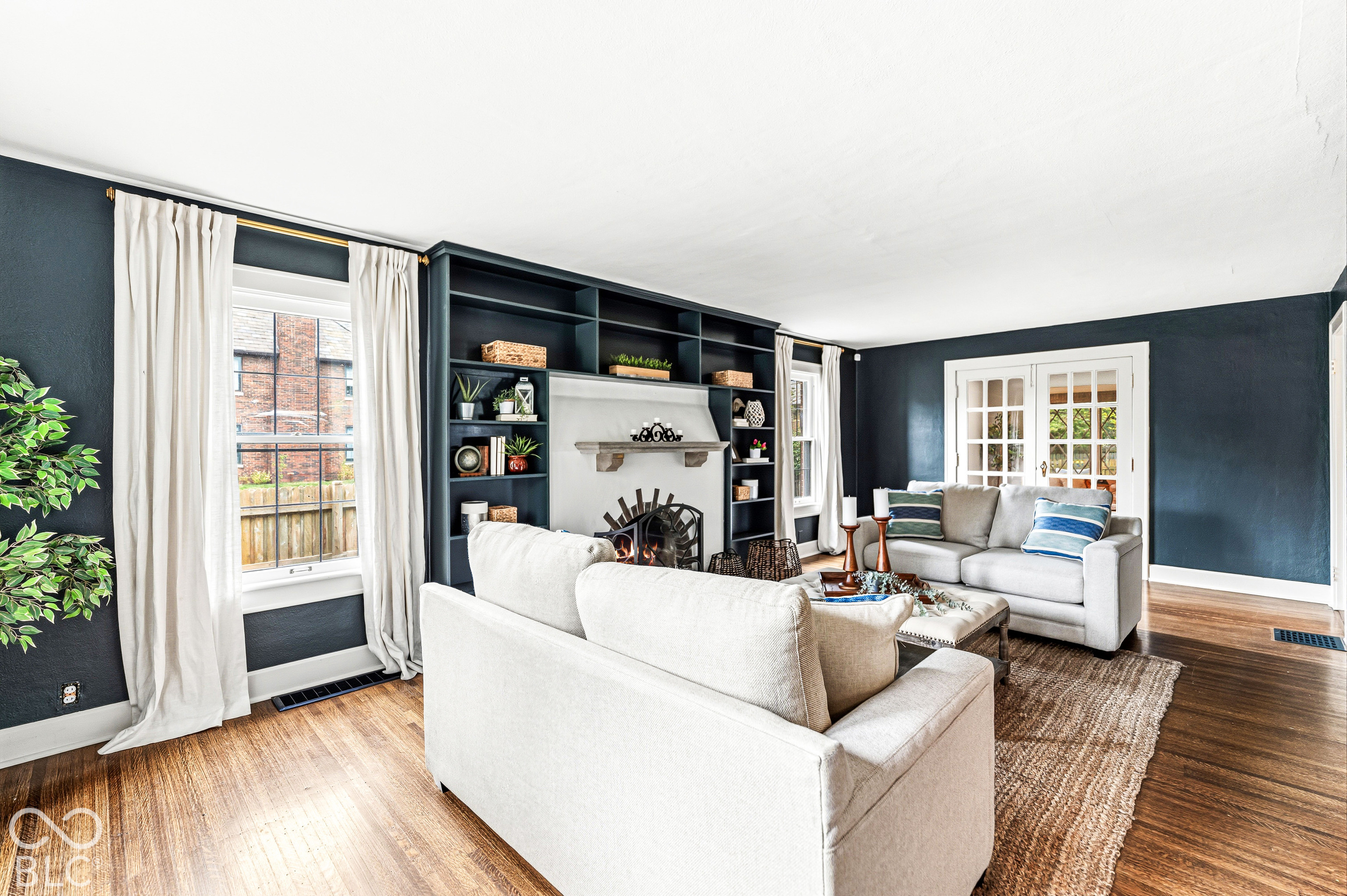 Living room featuring built-in dark cabinetry with integrated shelving, fireplace with a mantle, wood-finish flooring, and French doors