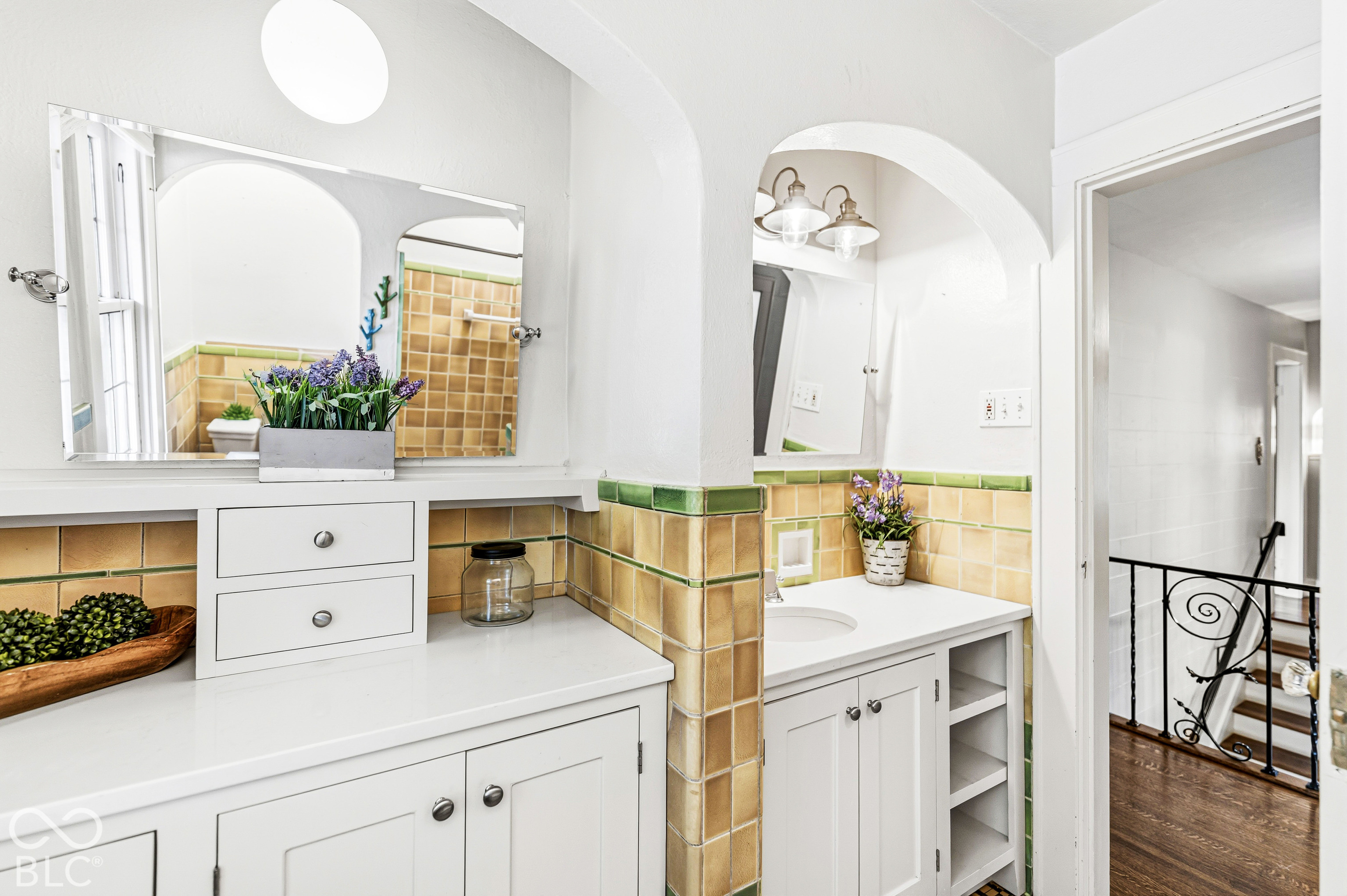Bathroom featuring white cabinetry, light-toned countertop, arched wall alcove, and decorative tile backsplash with green accents