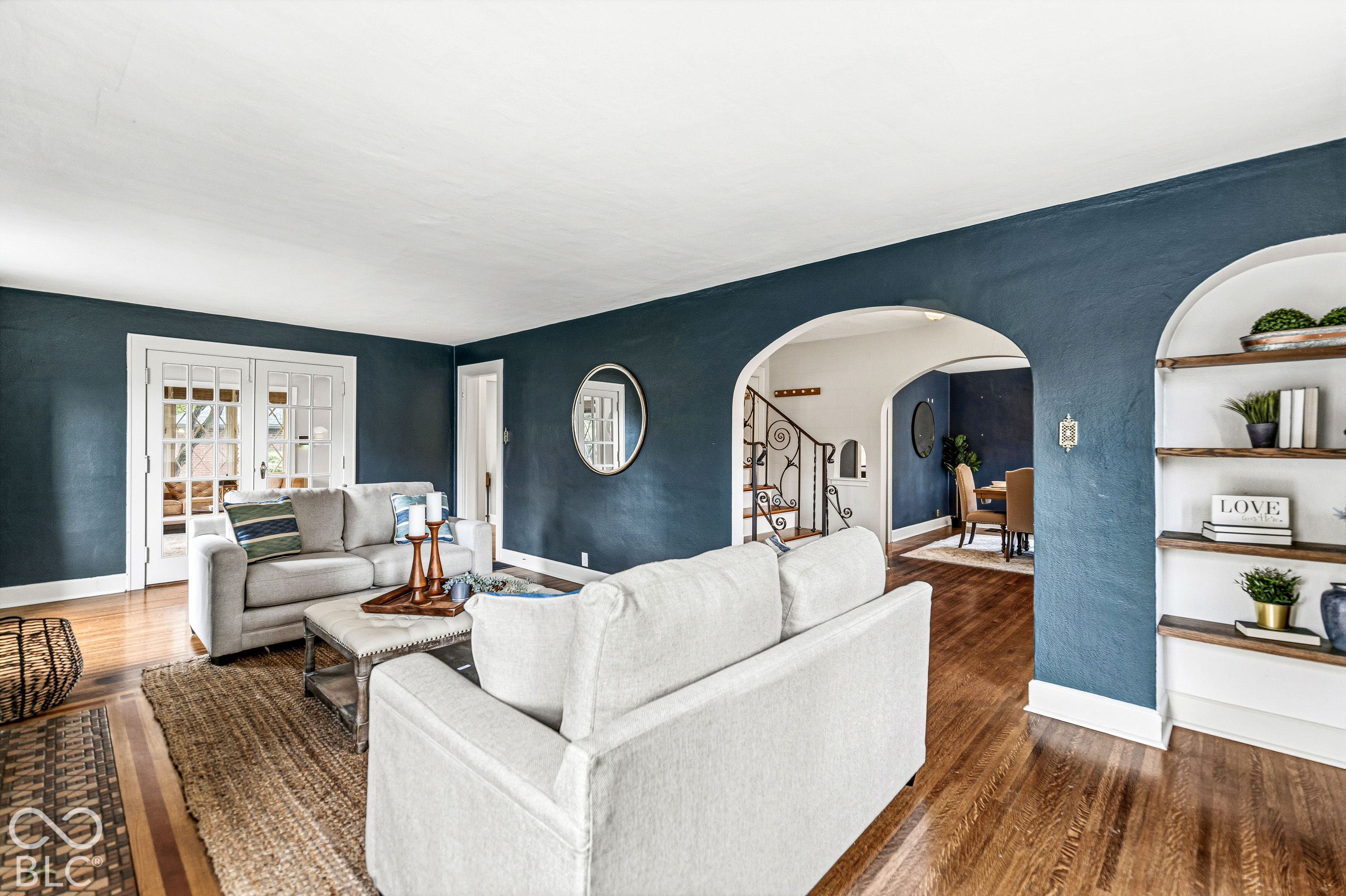 Living area featuring wood-finish flooring, recessed arched wall shelving, dual French doors, and distinctive arched architectural entryways