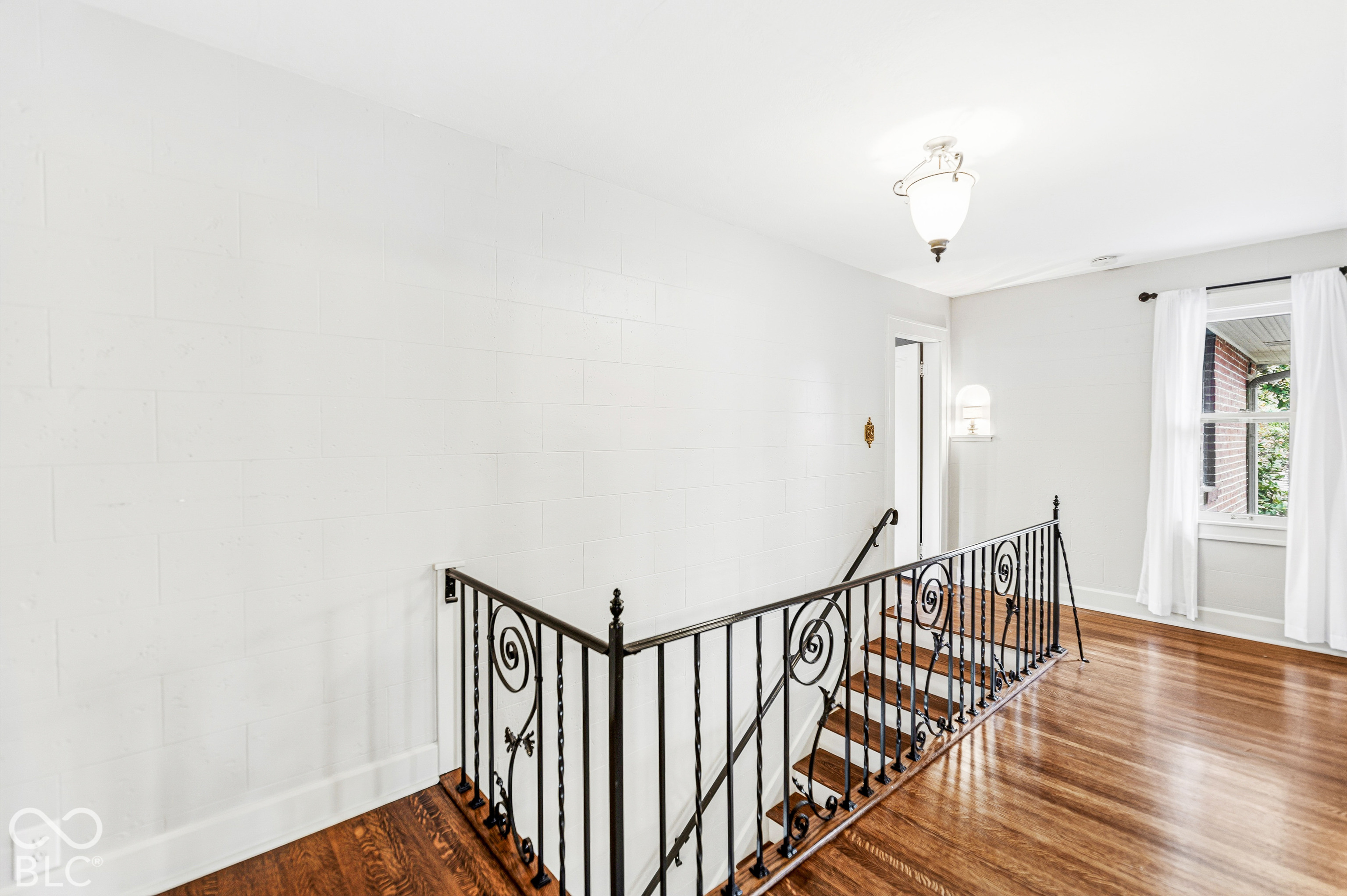 Wood-finish flooring, decorative wrought iron staircase railing, and pendant lighting
